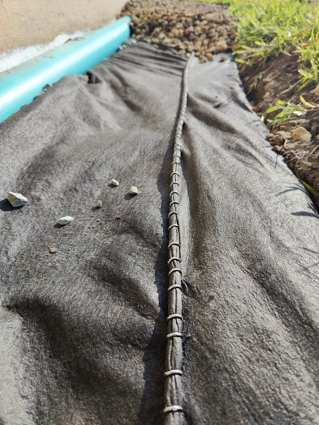 Trufam foundation drain wrapped in drainage fabric and stapled closed with a downspout line running along it in Tampa Bay