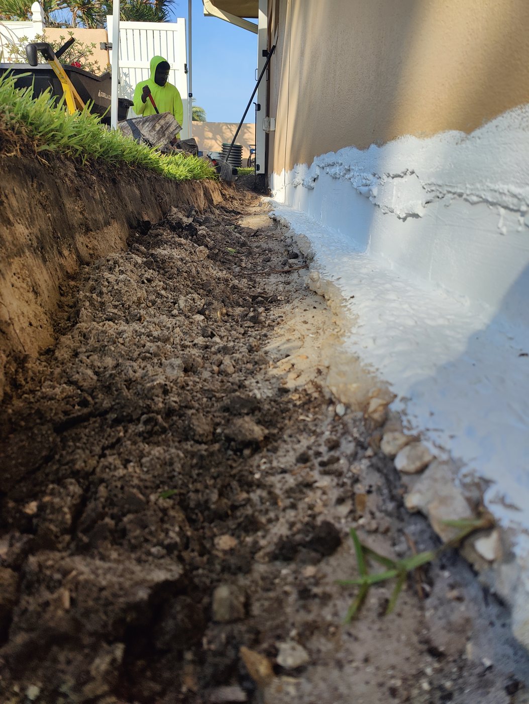 Looking down a foundation drain trench along a Tampa Bay home with the waterproofing coating already applied by Trufam Drainage