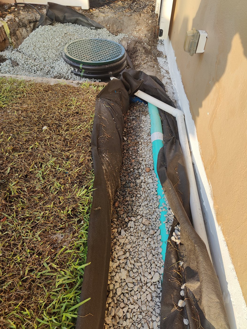 Trufam foundation drain in drainage fabric and #57 granite with a downspout line and a sump system, the waterproofing coating visible on the wall, in Tampa Bay