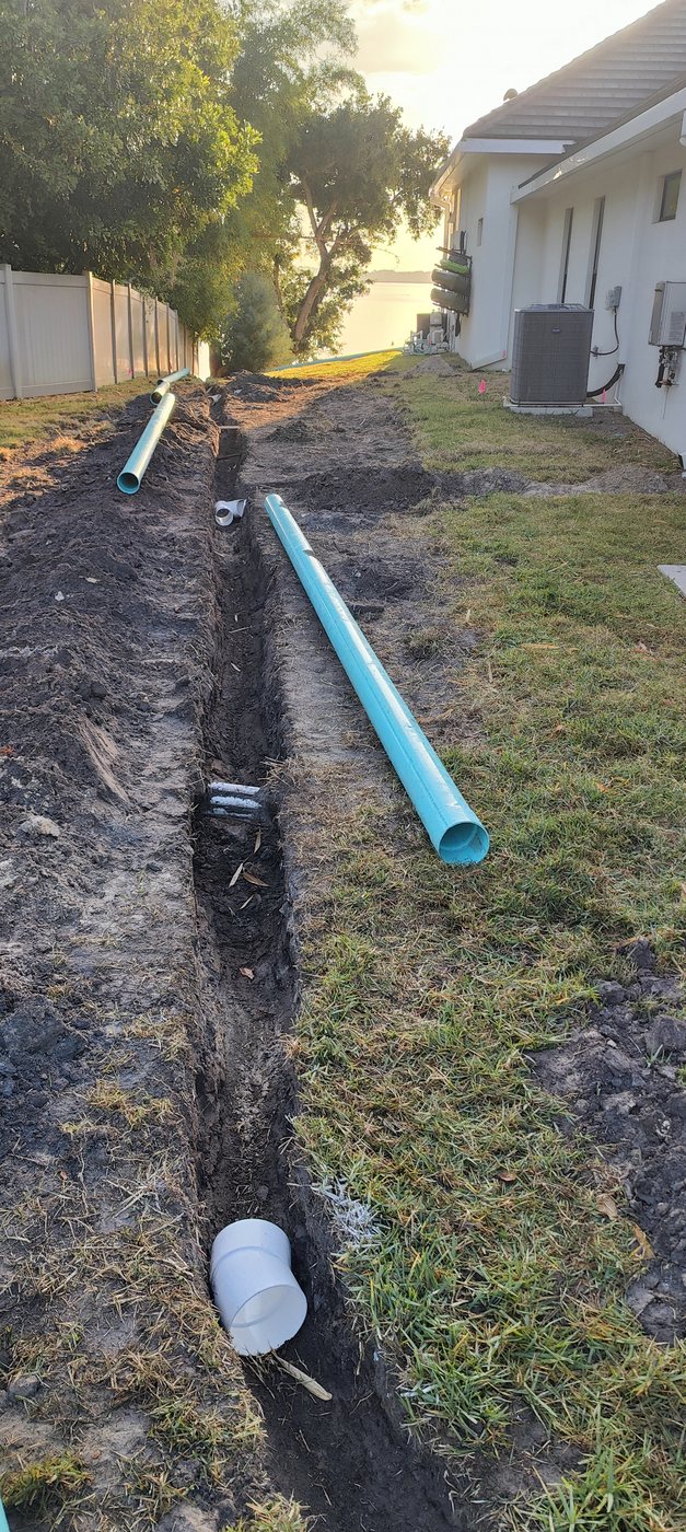 Solid SDR-35 drainage pipe staged beside a freshly dug trench for a Trufam underground drainage installation in Tampa Bay