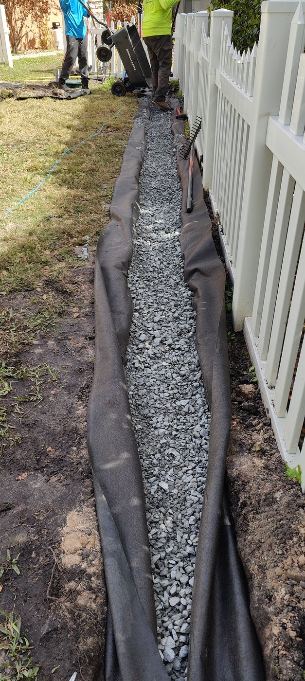 A Trufam yard drainage trench filled with clean gravel along a fence line in Tampa Bay