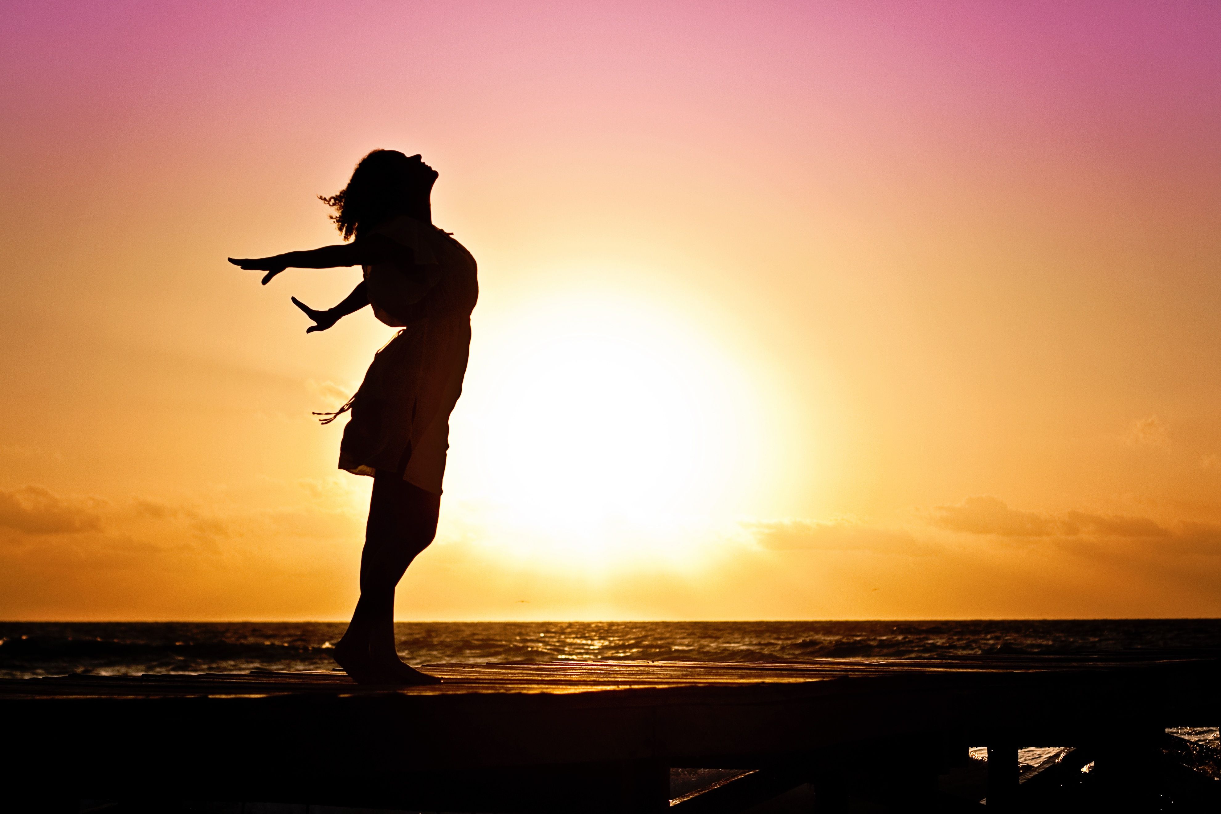Silhouette of a carefree woman with pink and orange sky background Silhouette of a carefree woman with pink and orange sky background