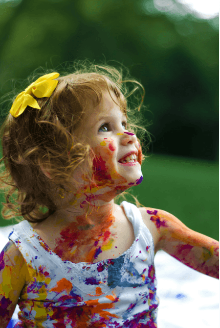 A girl playing outside with finger paint, seeing clearly with healthy eyes after receiving a pediatric eye exam