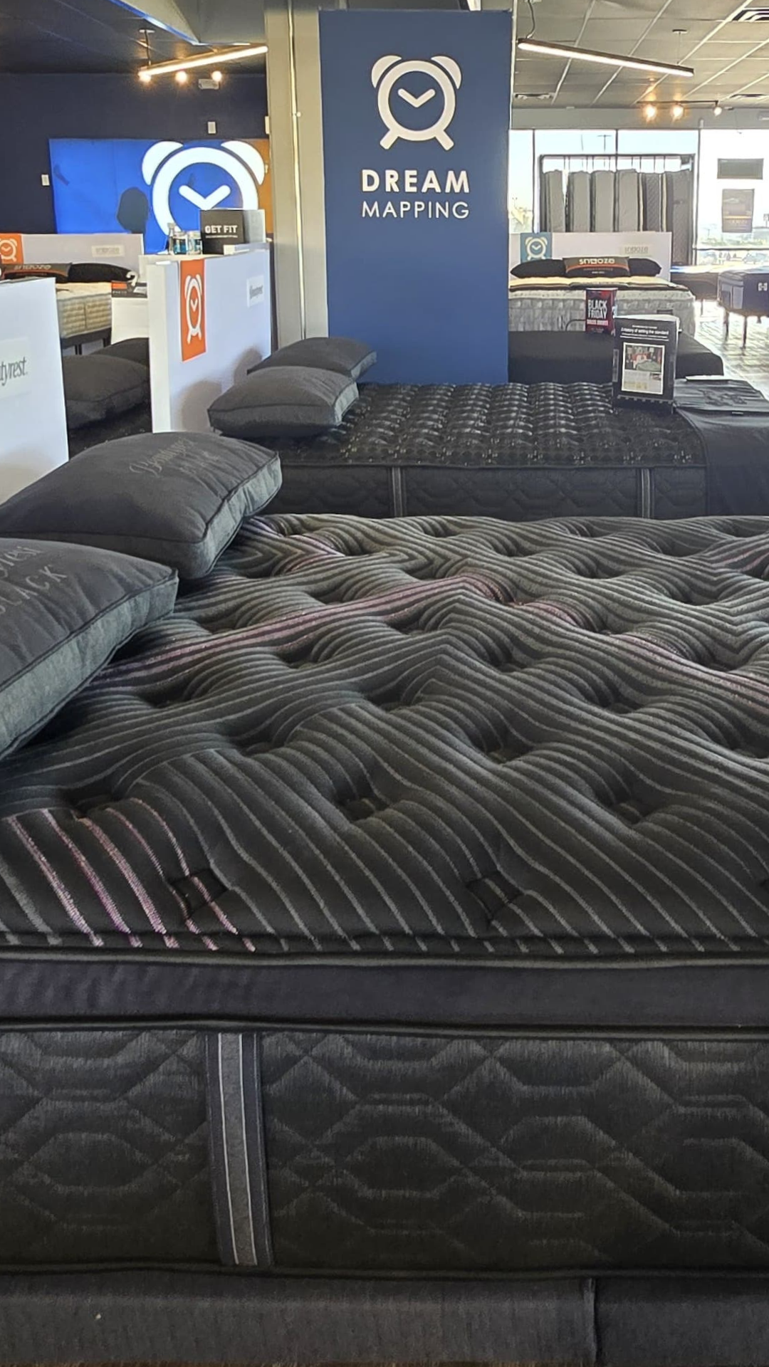 Showroom view of luxury black mattresses with pillows at Snooze Mattress + Wellness East El Paso, featuring Dream Mapping Technology display in the background.