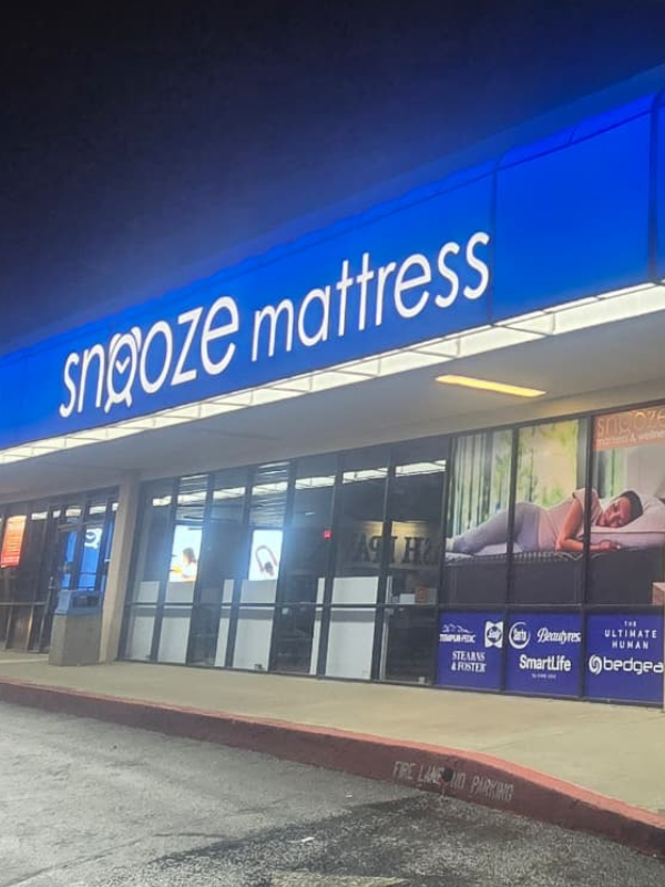 Snooze Mattress + Wellness storefront at night in East El Paso, featuring illuminated signage and window displays with premium mattress brands.