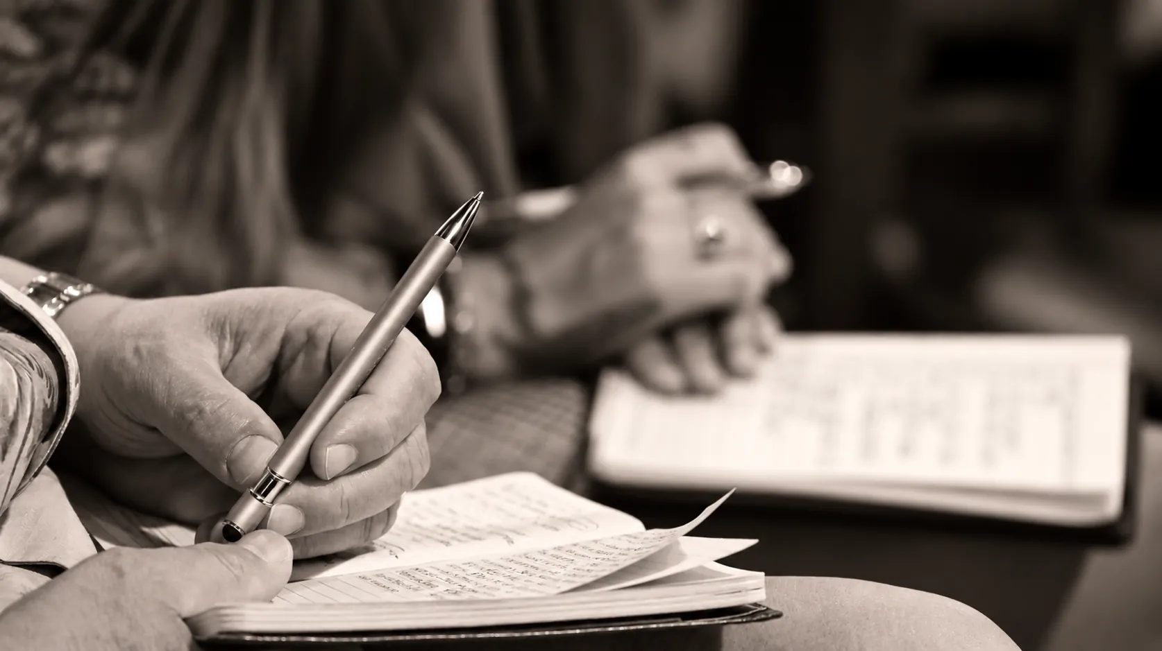 A hand writing with a pen in an open notebook