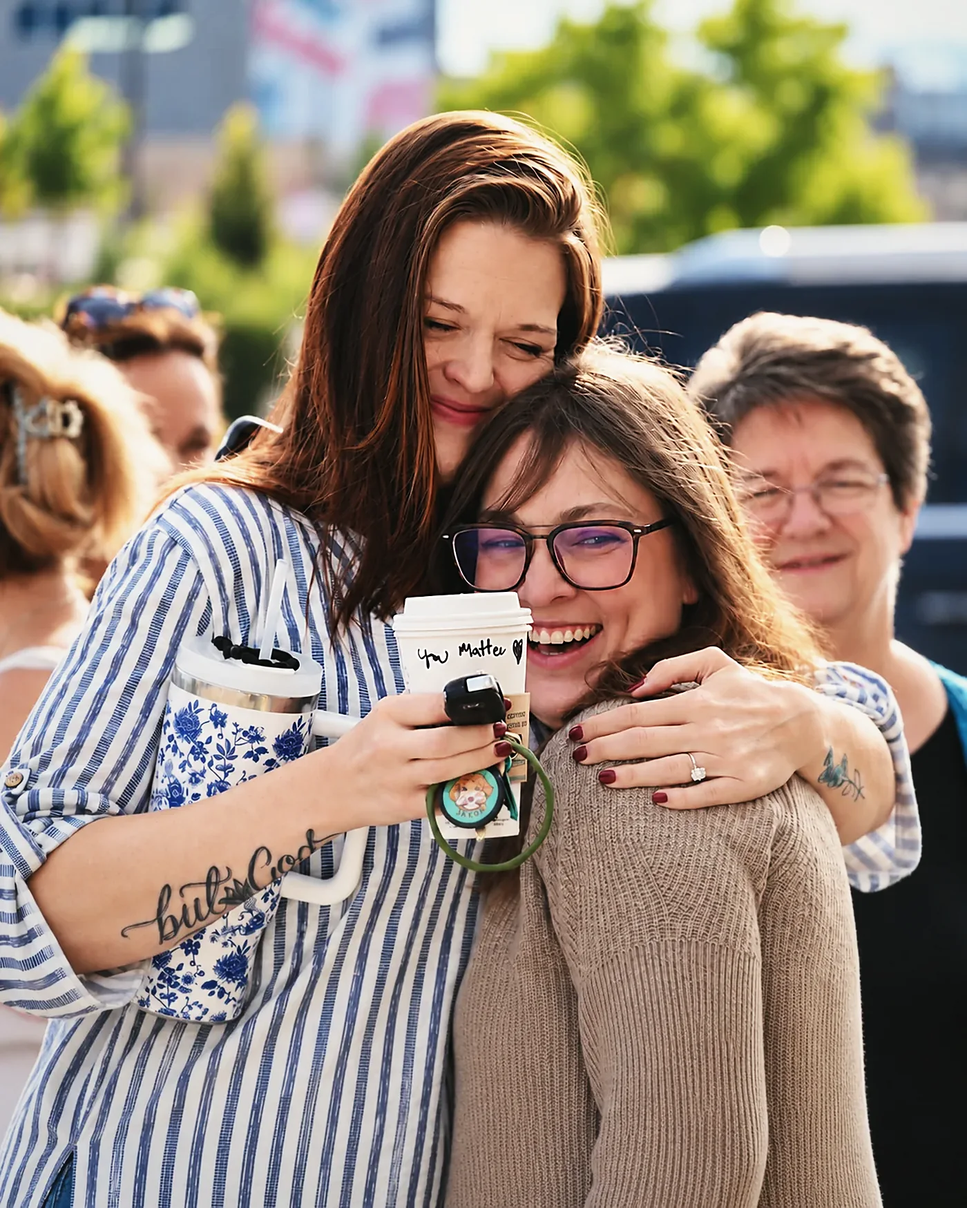 Two women from The Village Church share a warm embrace outside, one holding a coffee cup marked You Matter.