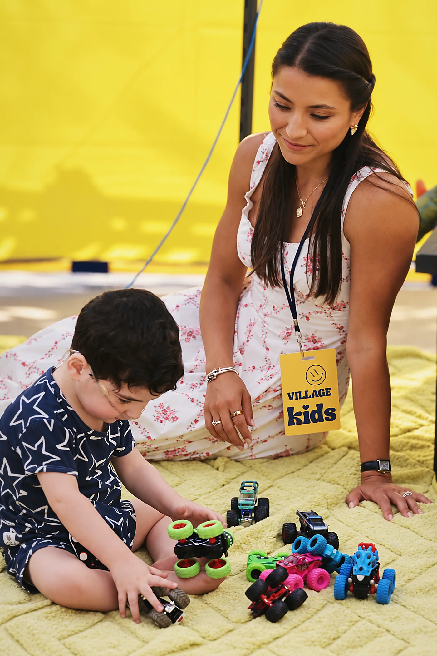 A Village Kids volunteer wearing her badge plays with a young child and a set of toy trucks.