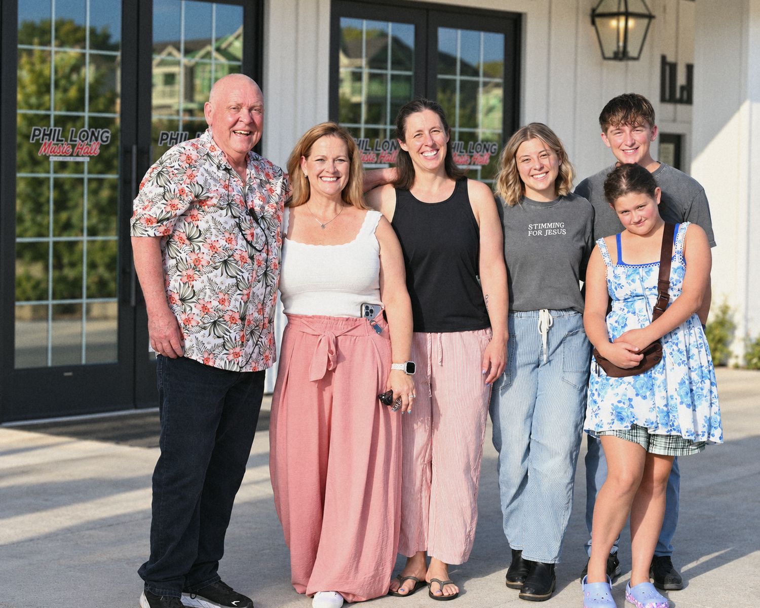 A family and friends smiling together outside the front doors of Phil Long Music Hall
