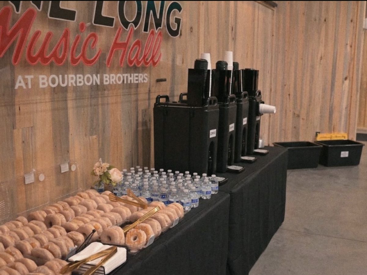 A welcome table with coffee, water, and donuts beneath the Phil Long Music Hall sign