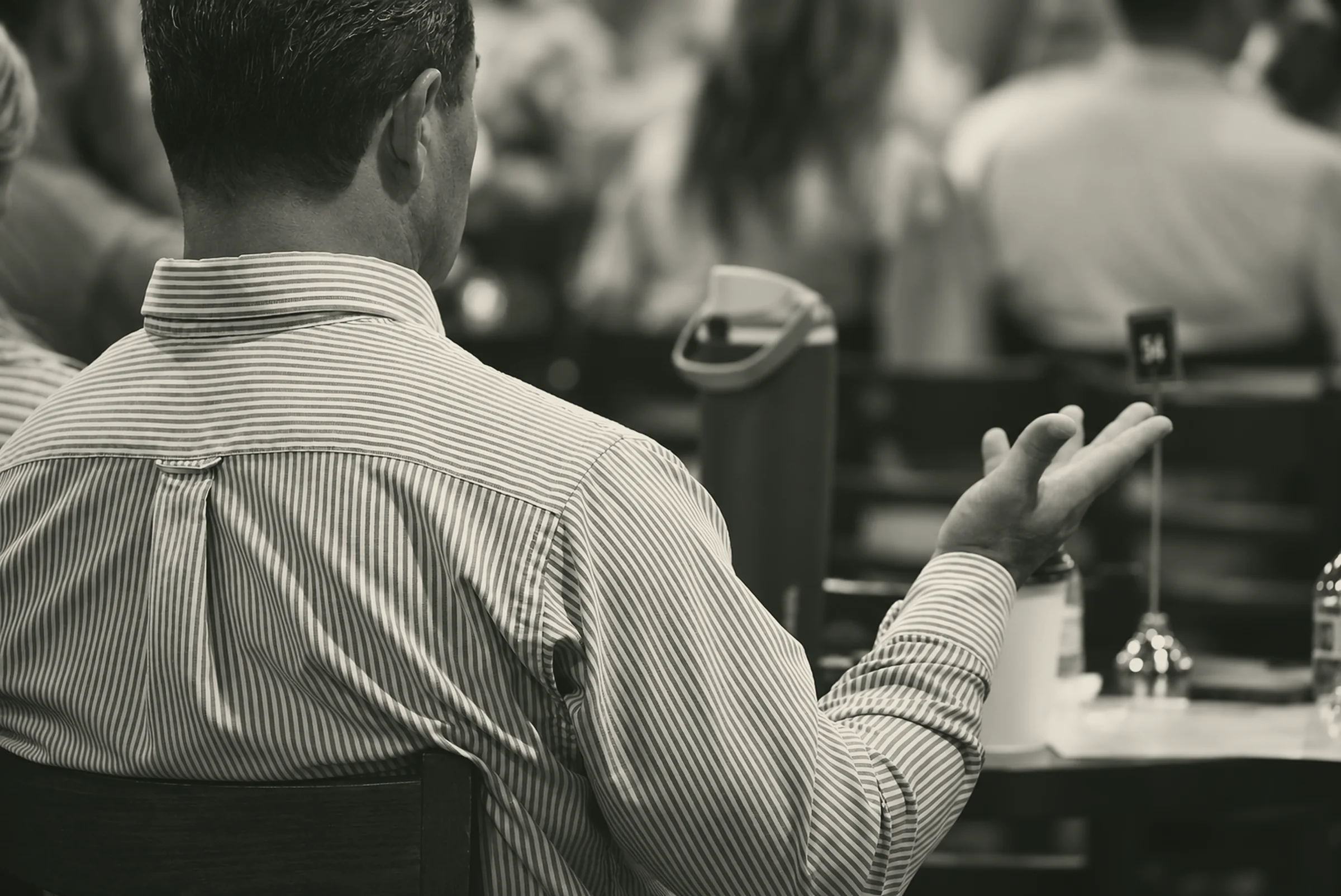 A man seated at a table during a Sunday gathering, his hand open mid-conversation