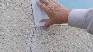 hand inspecting cracked stucco extending from window corner