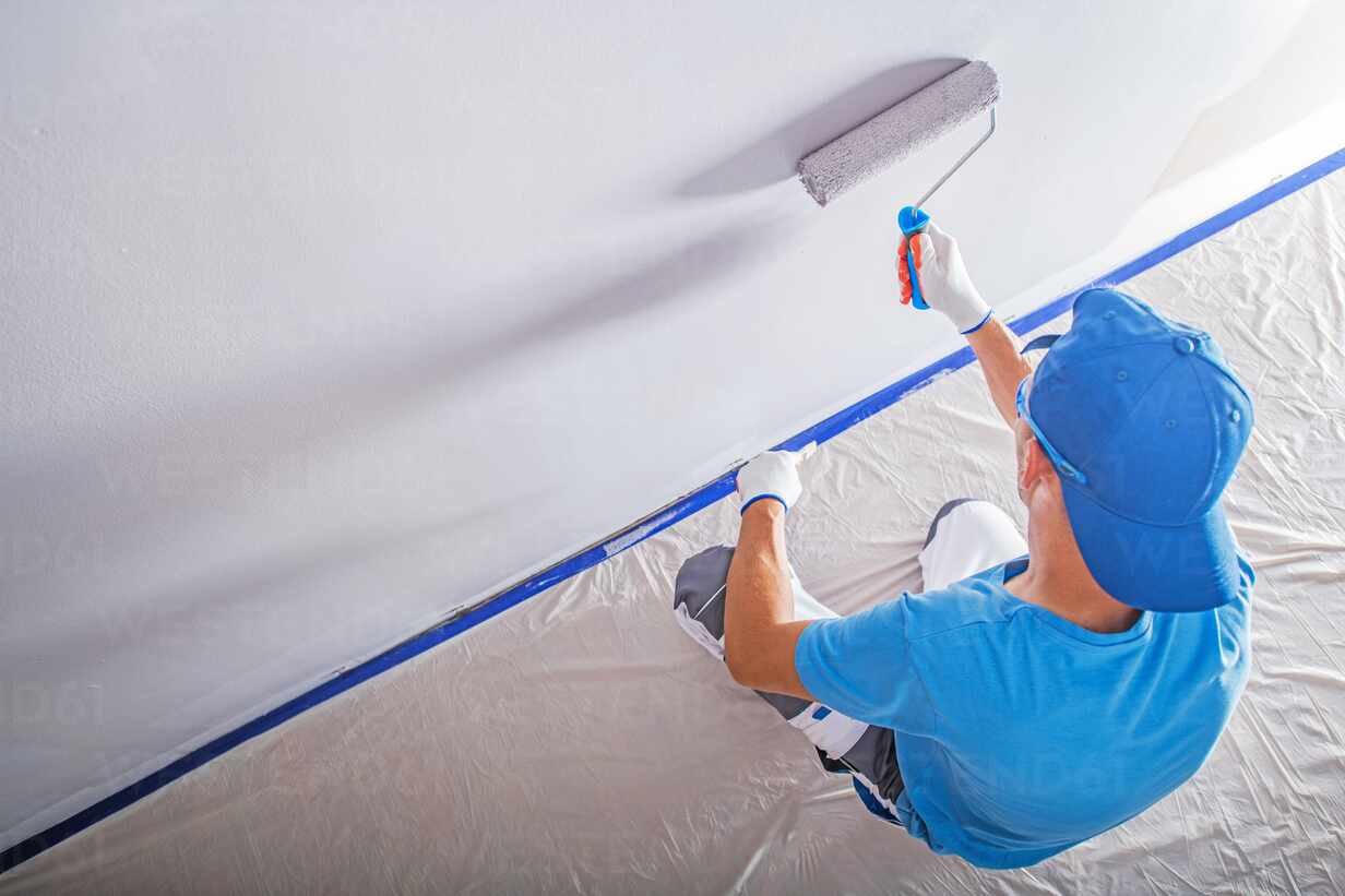 man painting hallway gray with roller