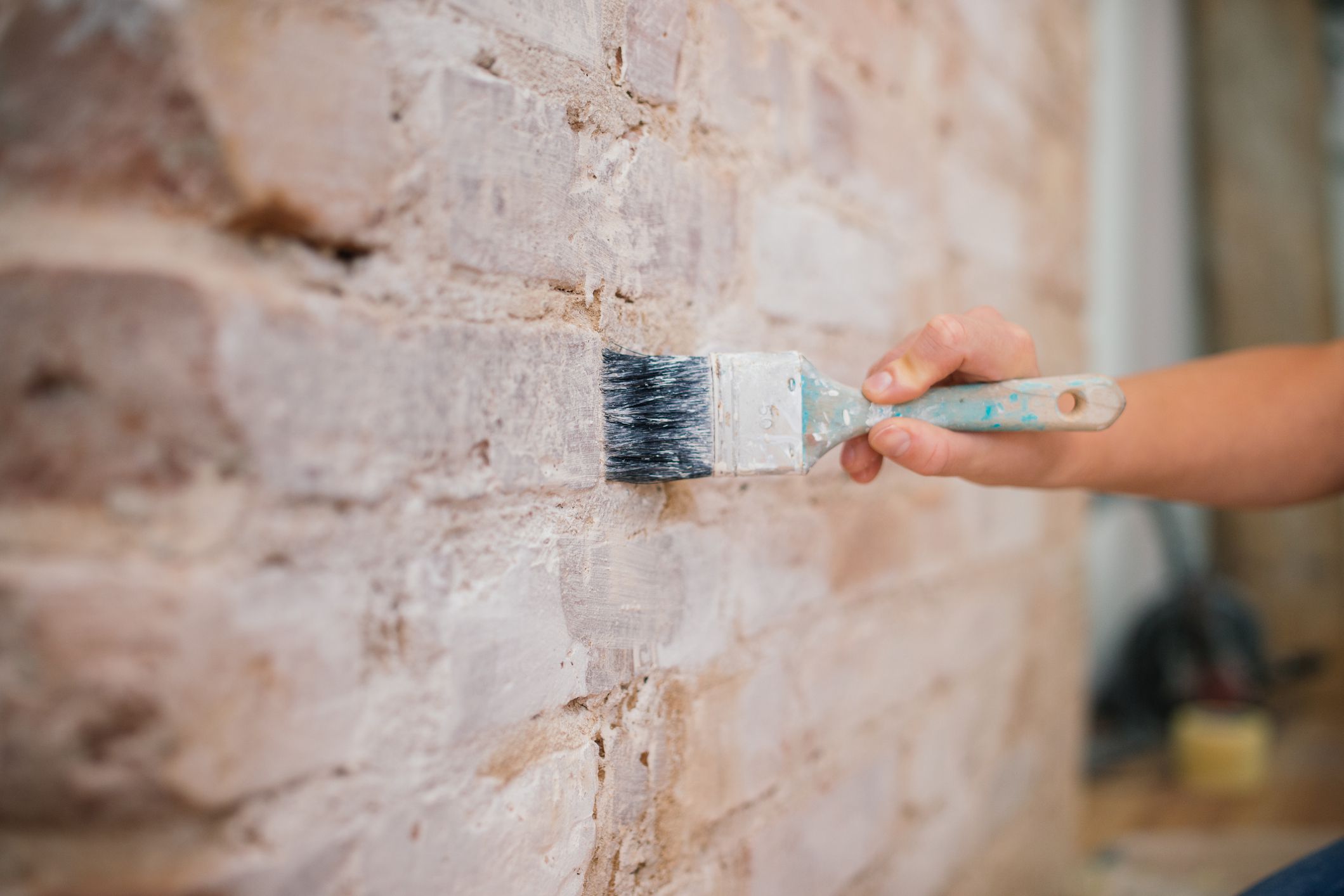 hand holding brush painting a brick wall