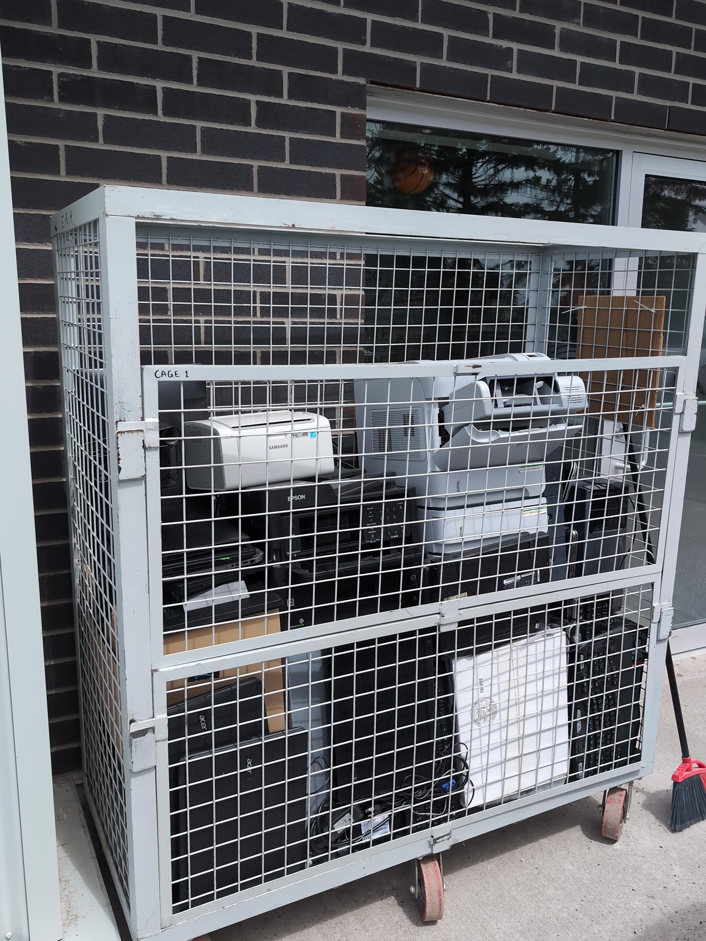 A large metal security cage filled with collected electronics, including printers and desktop towers, from a successful e-waste recycling event in Kanata.