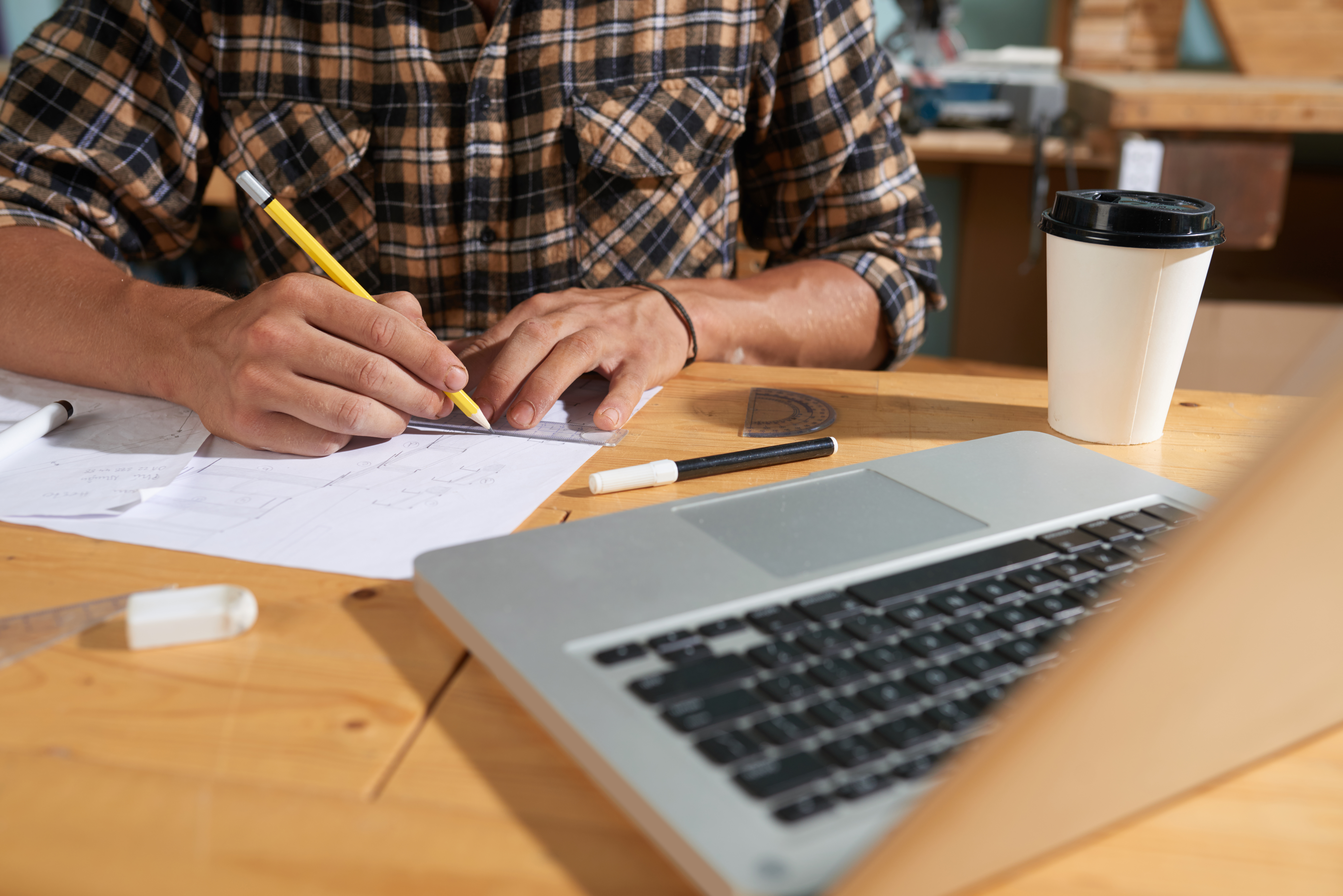 A close-up view of a professional working at a desk, reviewing blueprint schematics and project plans while utilizing a laptop. This represents Heartfelt IT's hands-on technical assessment, gap analysis, and infrastructure solution design support for nonprofit grant applications.