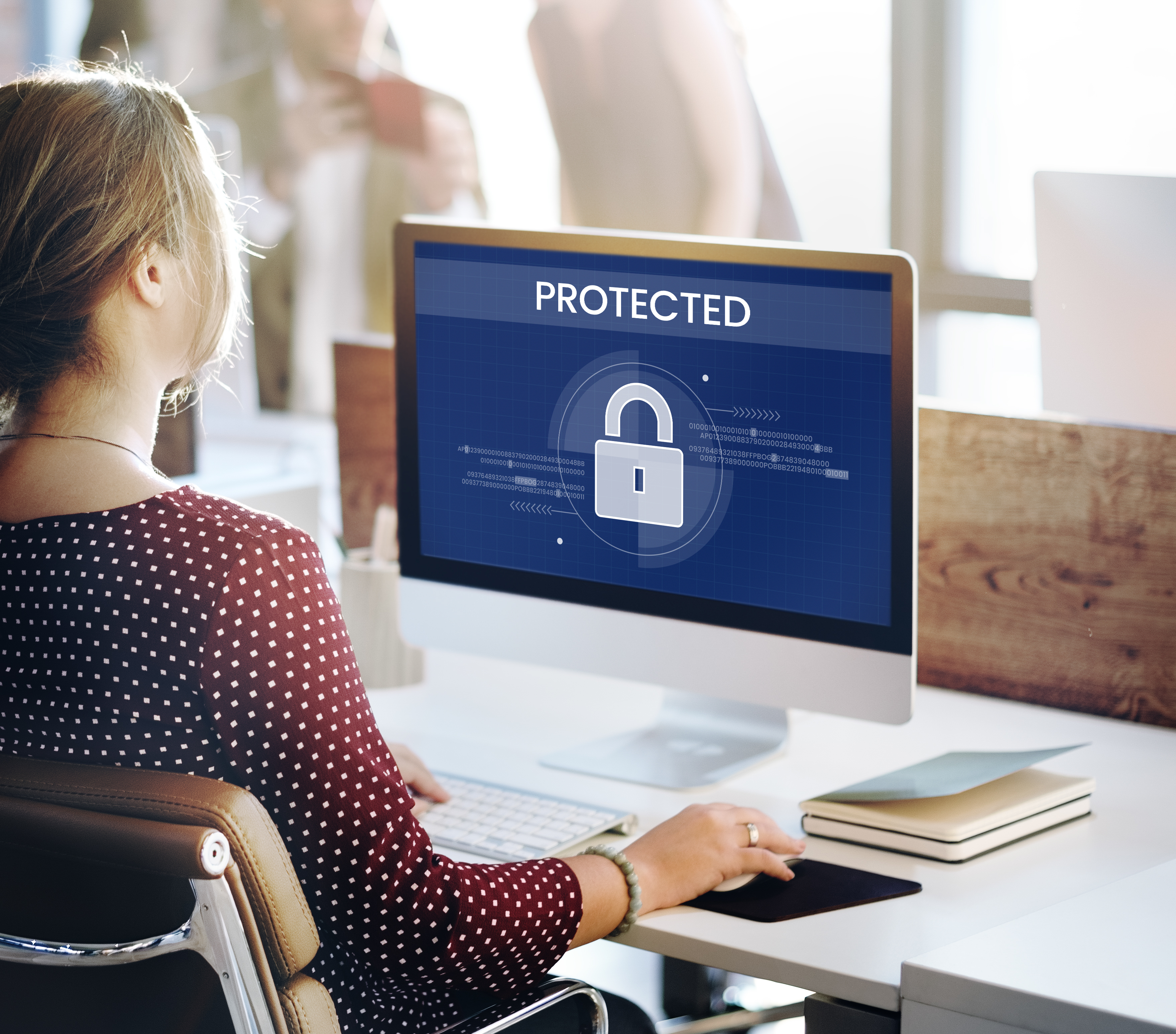 Office professional working at a desktop computer displaying a security lock icon and the word 'Protected,' representing advanced PC security, endpoint protection, and cybersecurity for business users