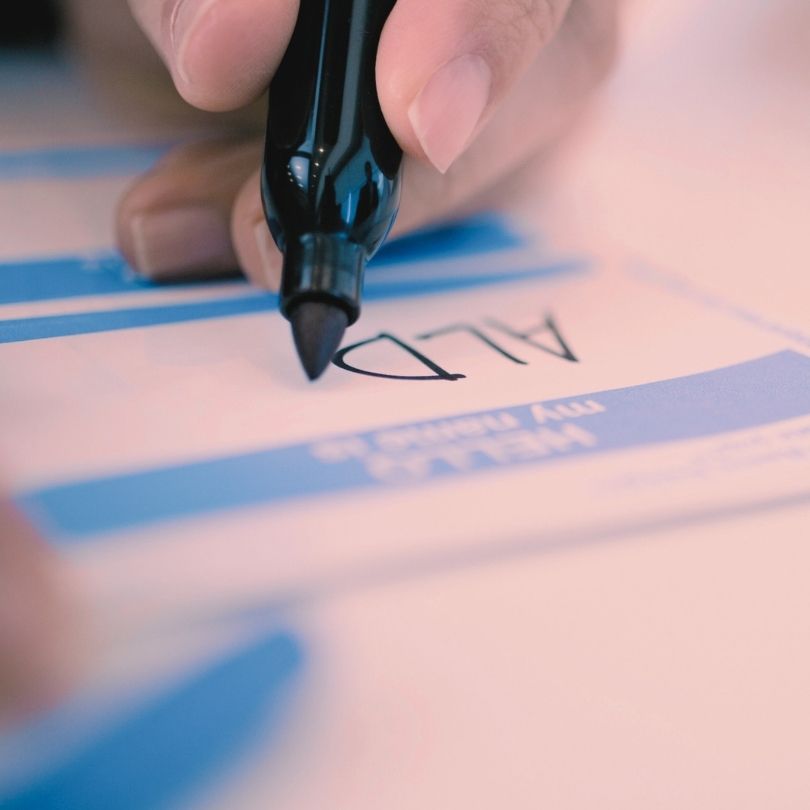 A hand writing a name on a name tag at the Agentic Think Tank check-in table