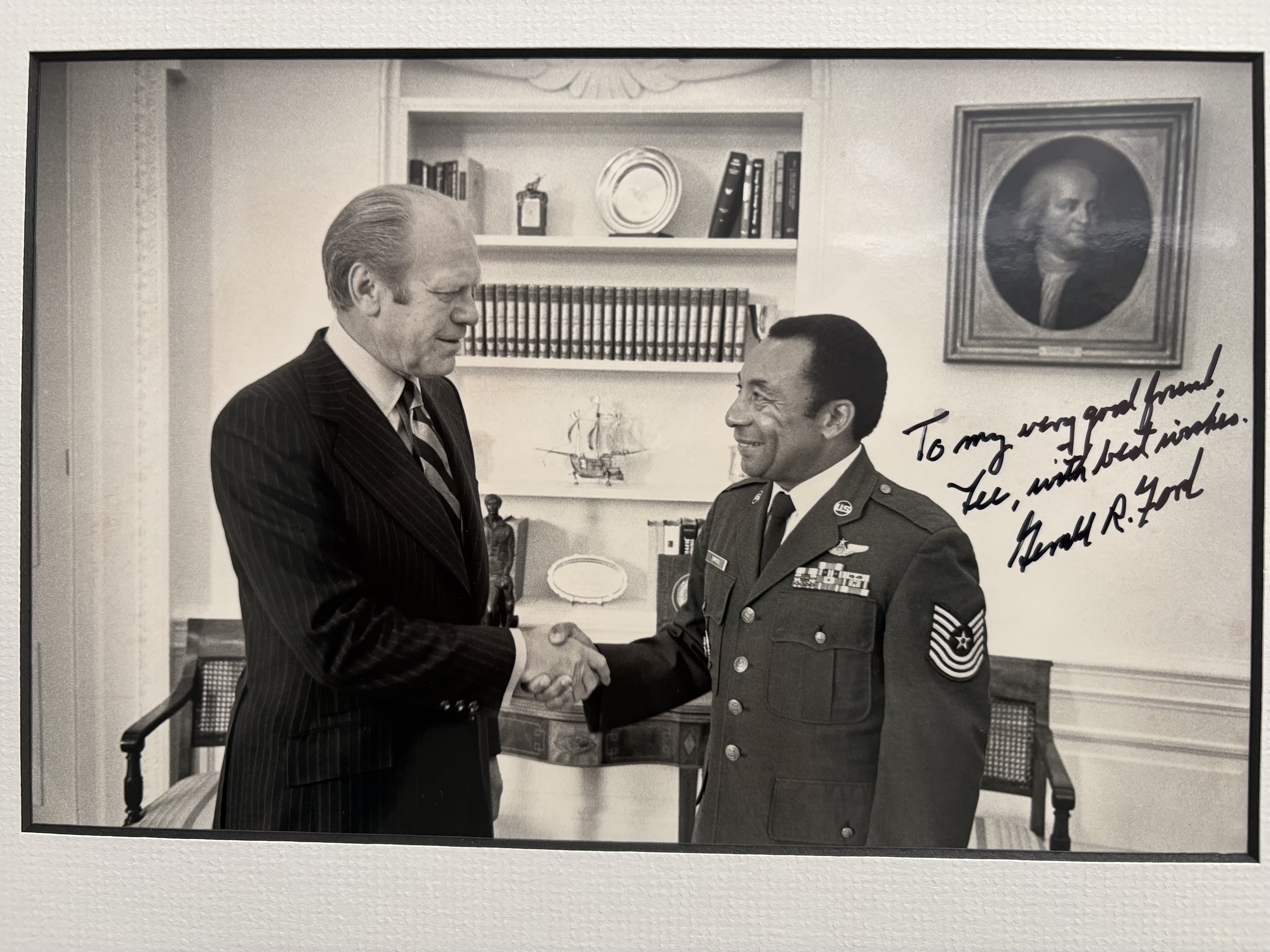 President Gerald R. Ford shaking hands with Lee F. Simmons in a presidential office. Simmons wears his Air Force Technical Sergeant dress uniform. The original print is inscribed by President Ford: To my very good friend, Lee, with best wishes — Gerald R. Ford.