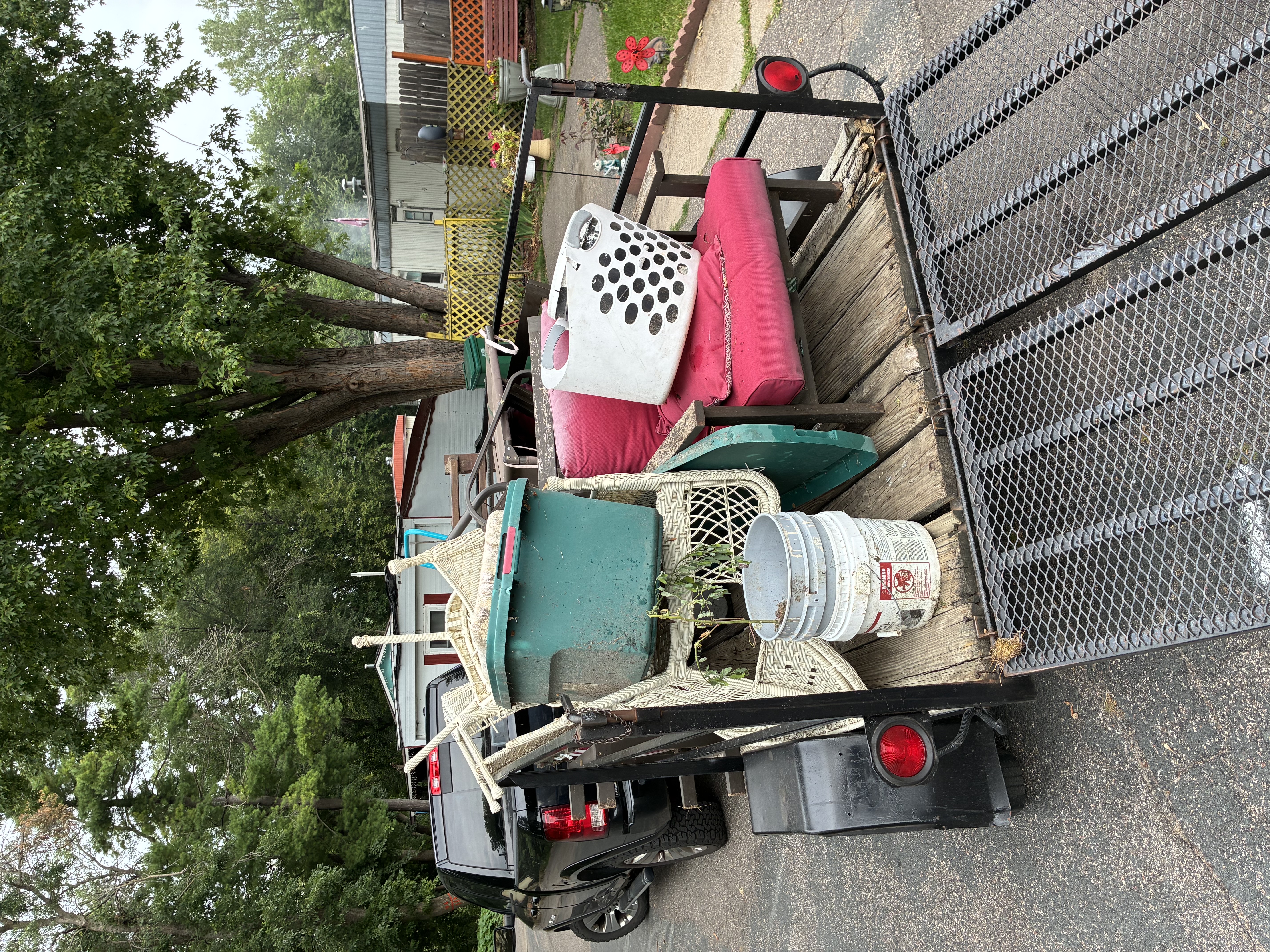 A NextGen Hauling trailer loaded with furniture, totes and yard debris, parked on a Bloomington street with the ramp down