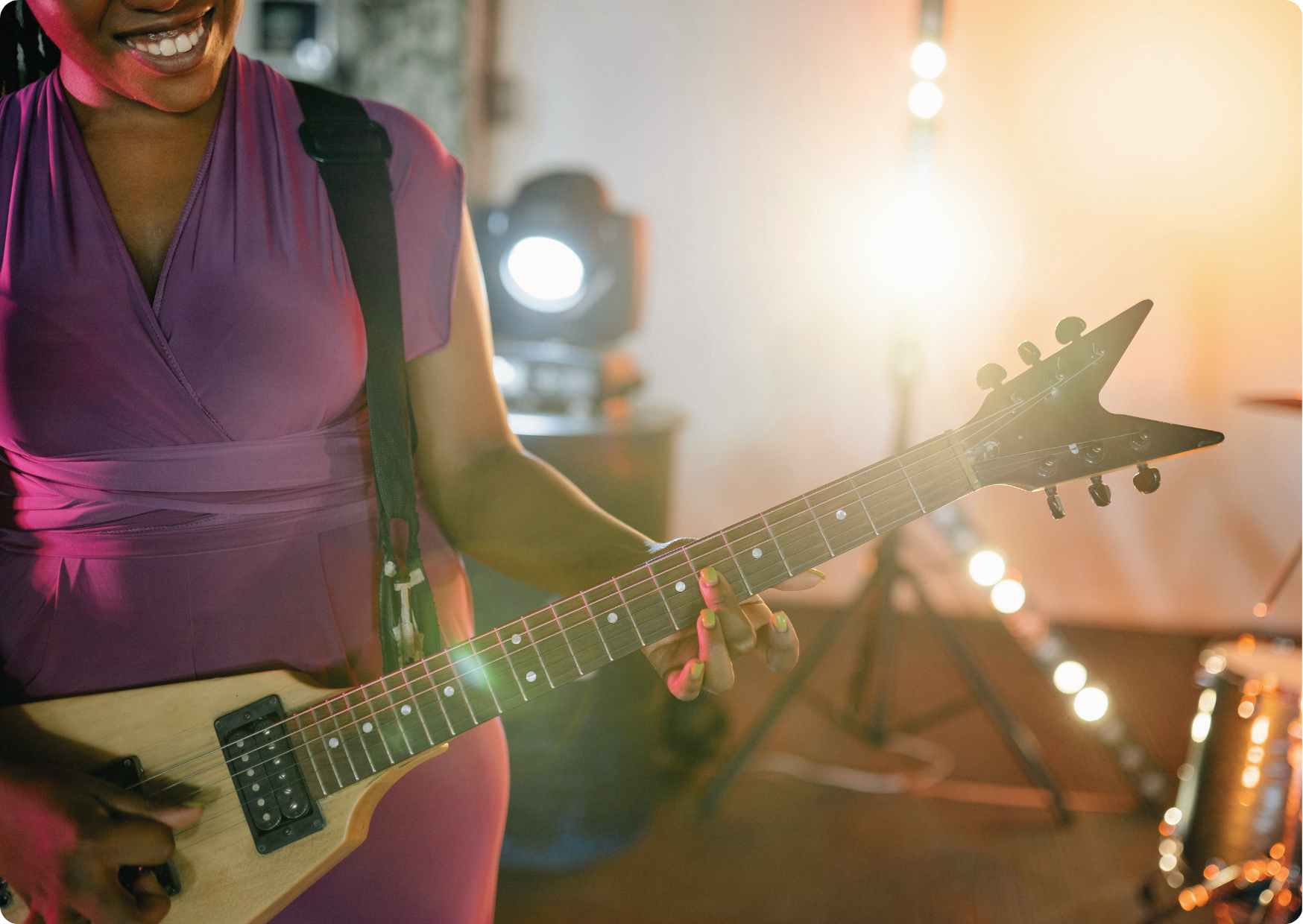 Blog Aude Compose - Afro-américaine dans une robe rose sourit sur scène et joue de la guitare électrique 