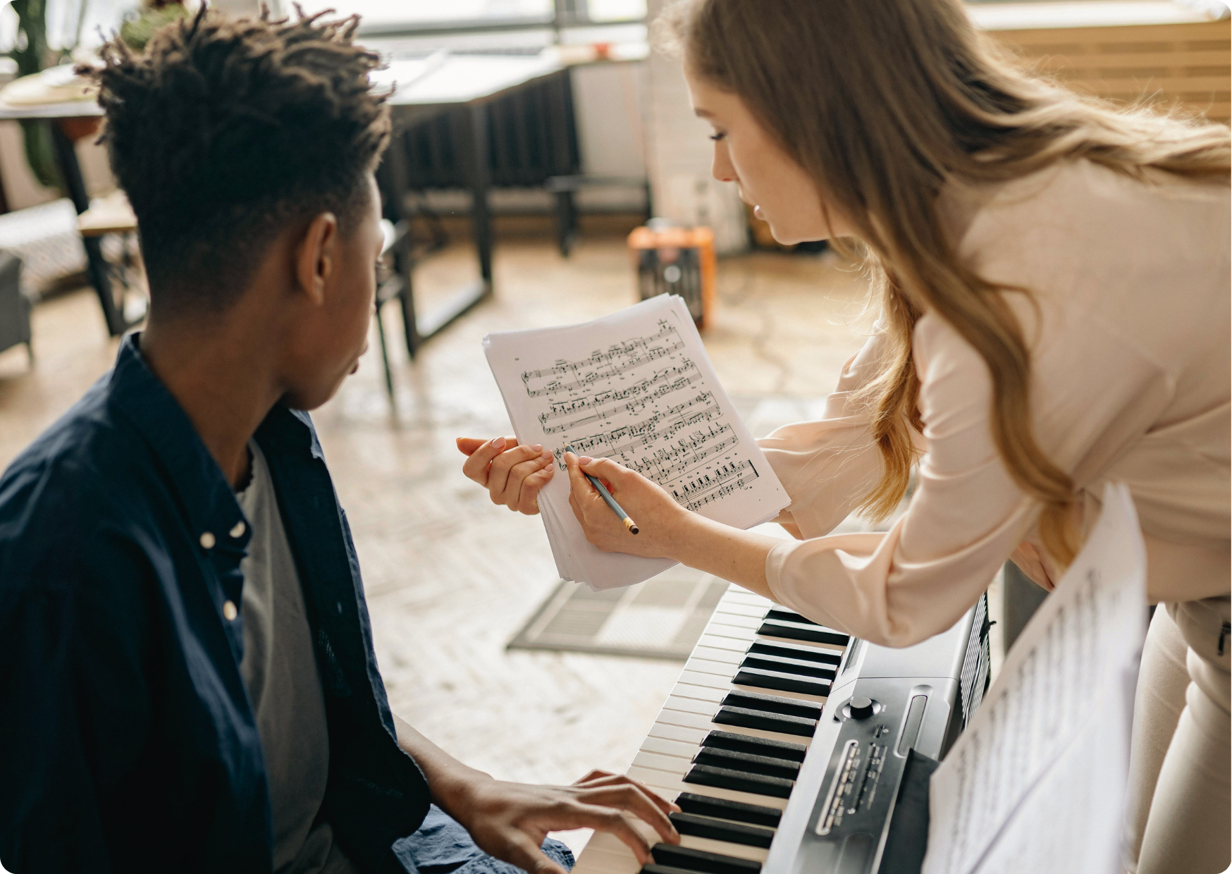 Blog Aude Compose - Professeure de piano aux cheveux blond vénitien explique une partition à un élève adolescent afro-américain