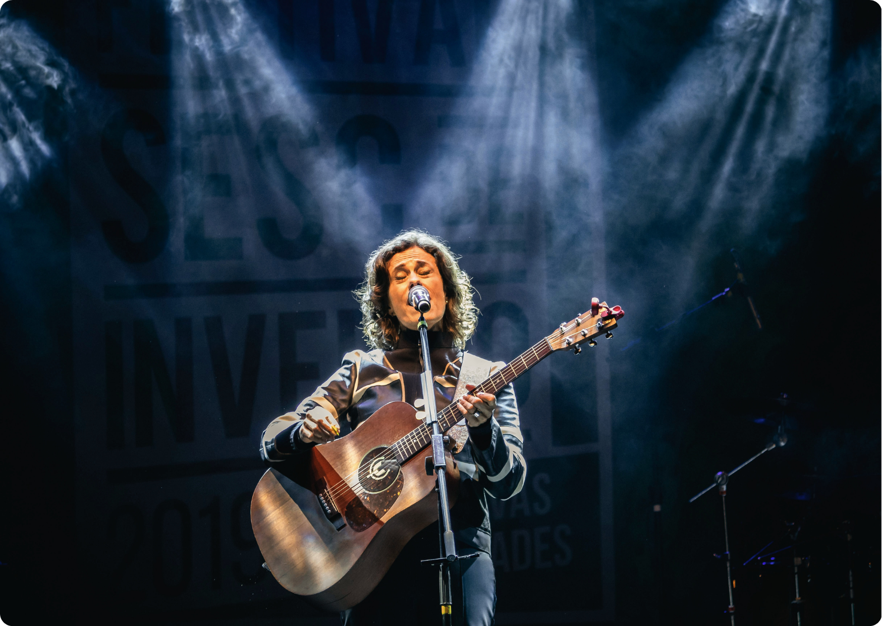 Blog Aude Compose - Femme âgée joue de la guitare et chante sous les projecteurs d'une scène