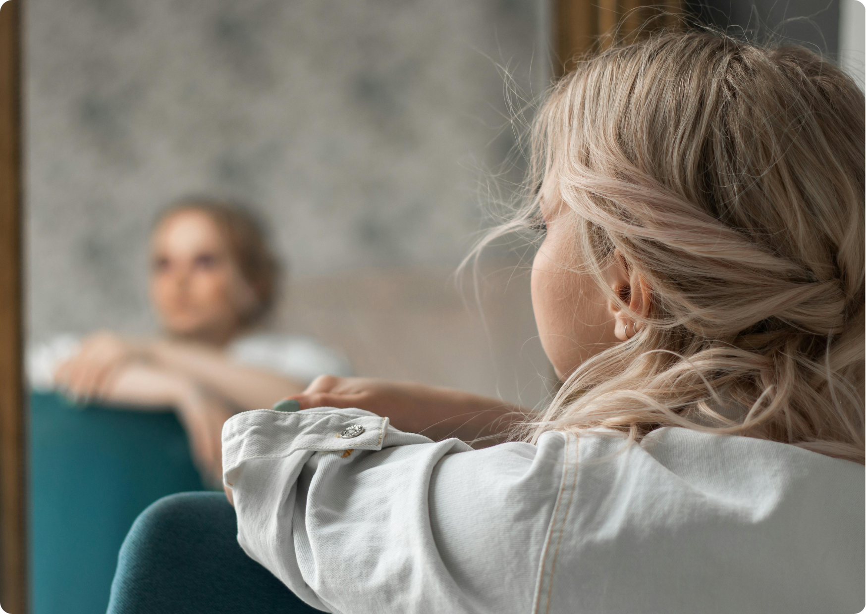 Blog Aude Compose - Femme blond cendré accoudée à un siège bleu canard, de do et son reflet flou dans un immense miroir
