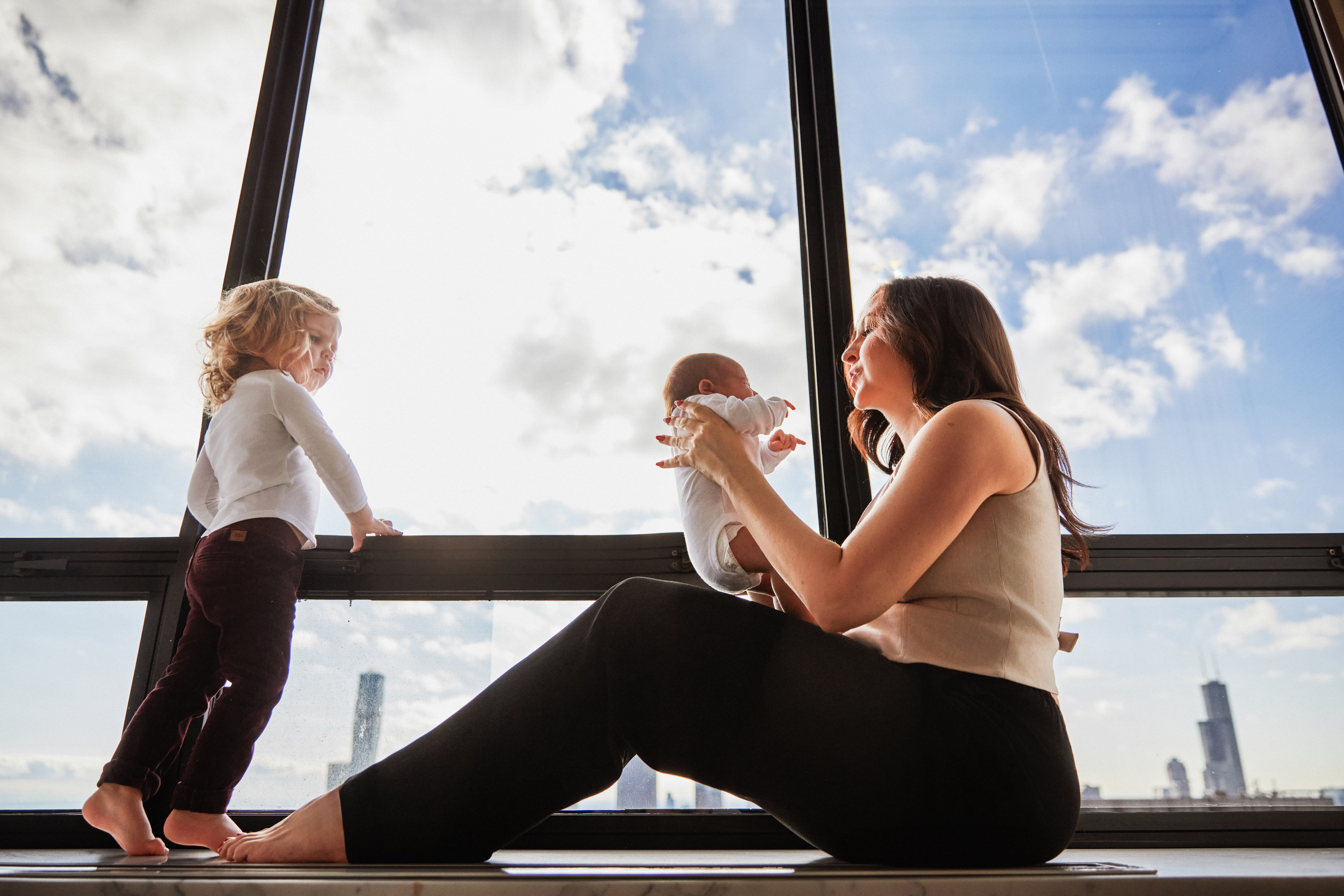Mother with newborn and toddler by high-rise window, Chicago skyline behind