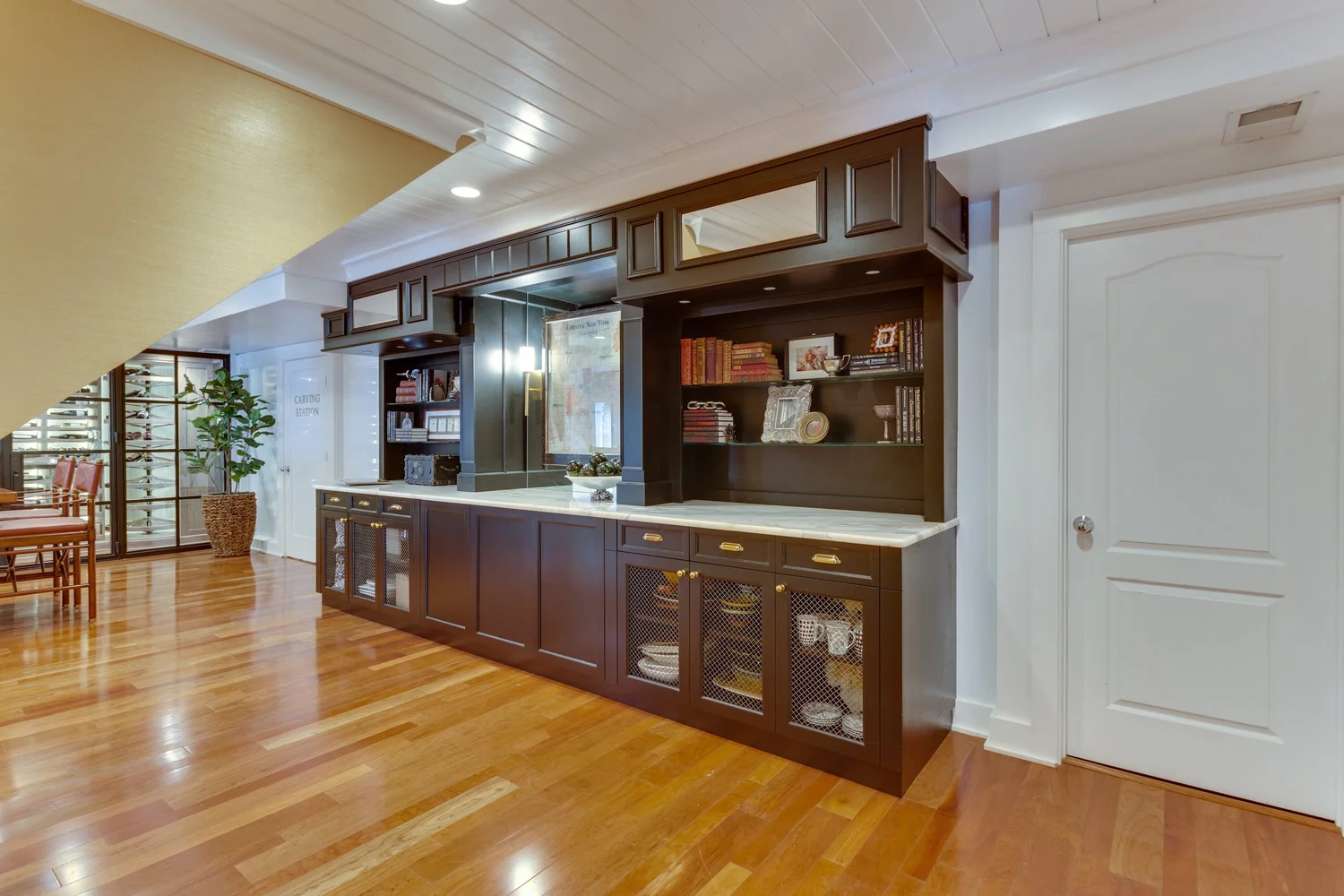 Custom furniture grade millwork wine cellar cabinetry installed in a formal McLean, Virginia home, featuring floor-to-ceiling hardwood racking, fitted crown molding, and integrated display lighting. The millwork aligns with the room's existing architectural trim and paneled walls.