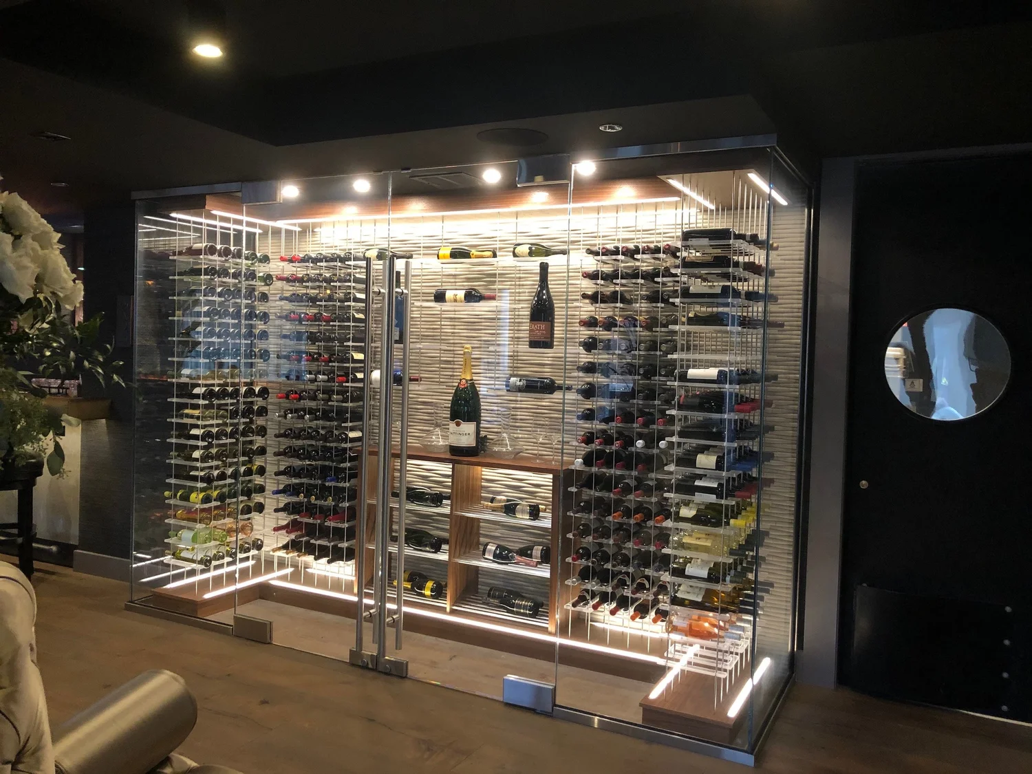 Modern luxury wine cellar with black cabinetry, gold accents, and burgundy lighting showcasing custom wine storage and upscale bar area