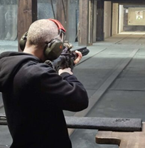Man in red baseball cap, shooting a gun toward a target in a gun range Man in red baseball cap, shooting a gun toward a target in a gun range