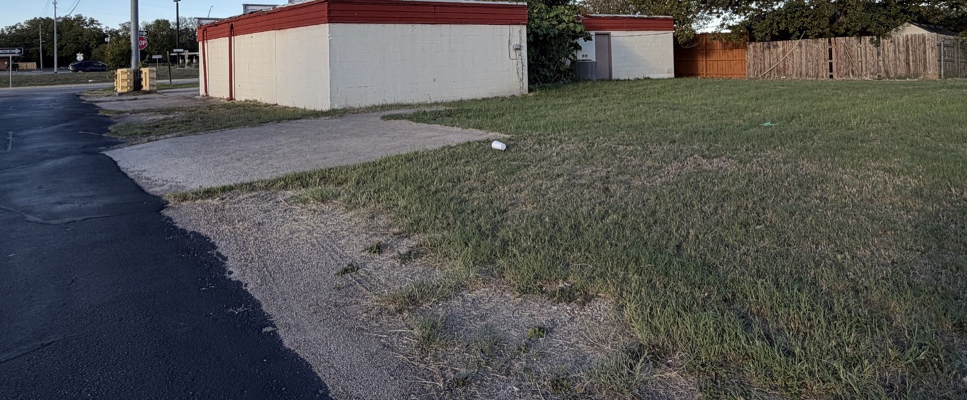 Open lawn at the corner of the lot with the building and fence in the background