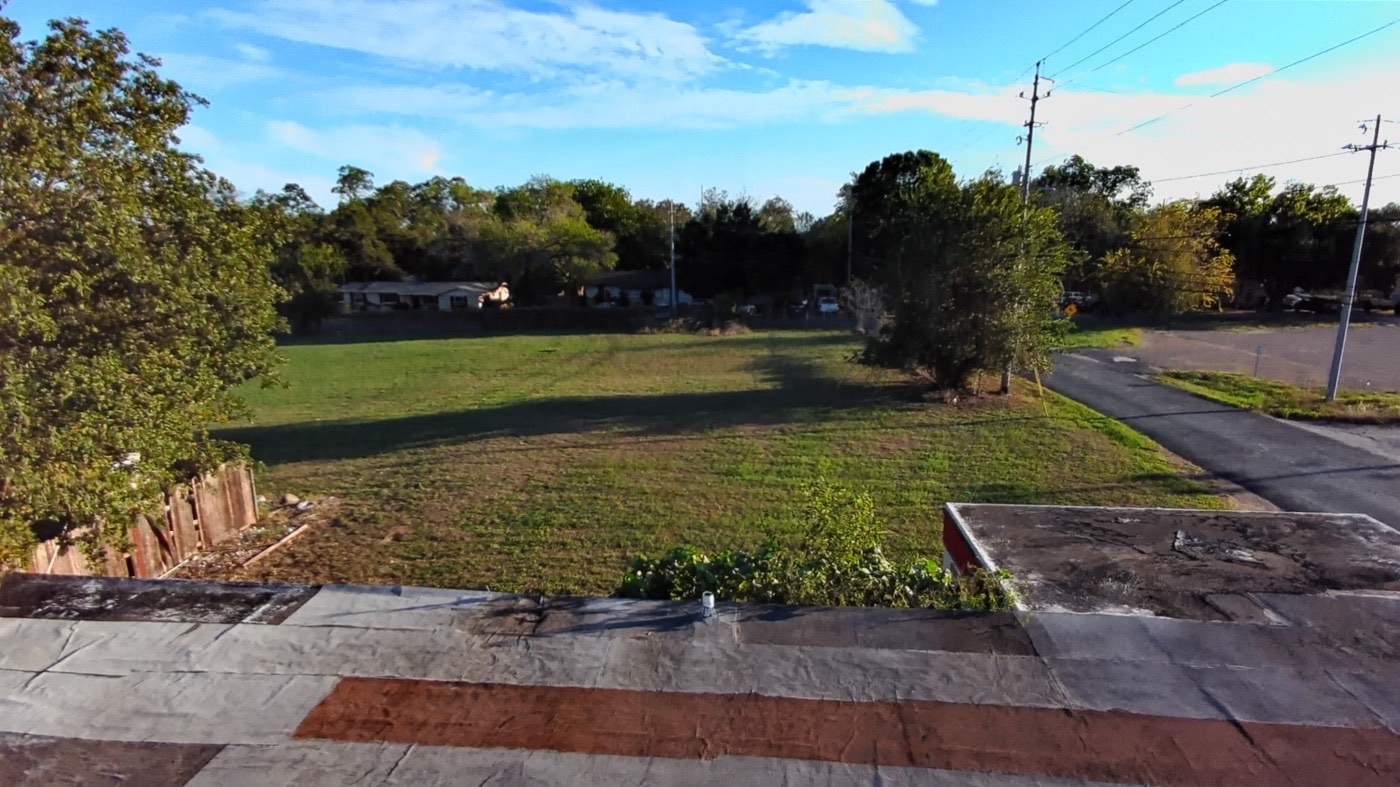 Aerial view from the roofline across the open grass lot and mature trees