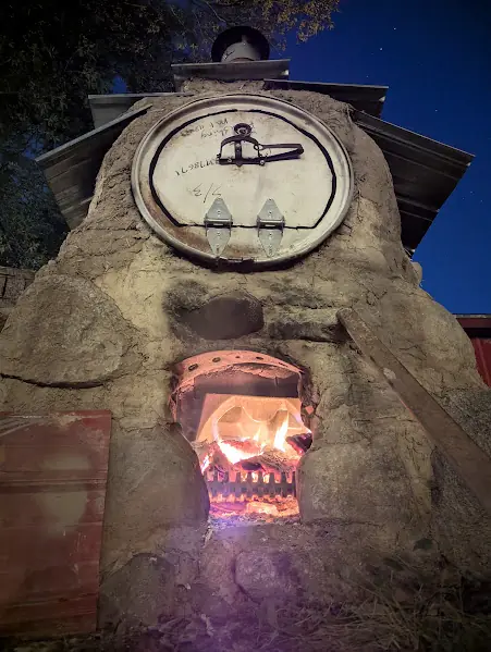 Renegade Sourdough's handbuilt wood-fired cob oven at night with a live fire burning in the firebox.