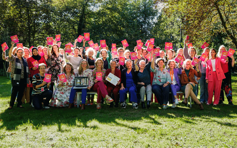 Jeanet Bathoorn met een grote groep klanten en het boek dat ze samen schreven