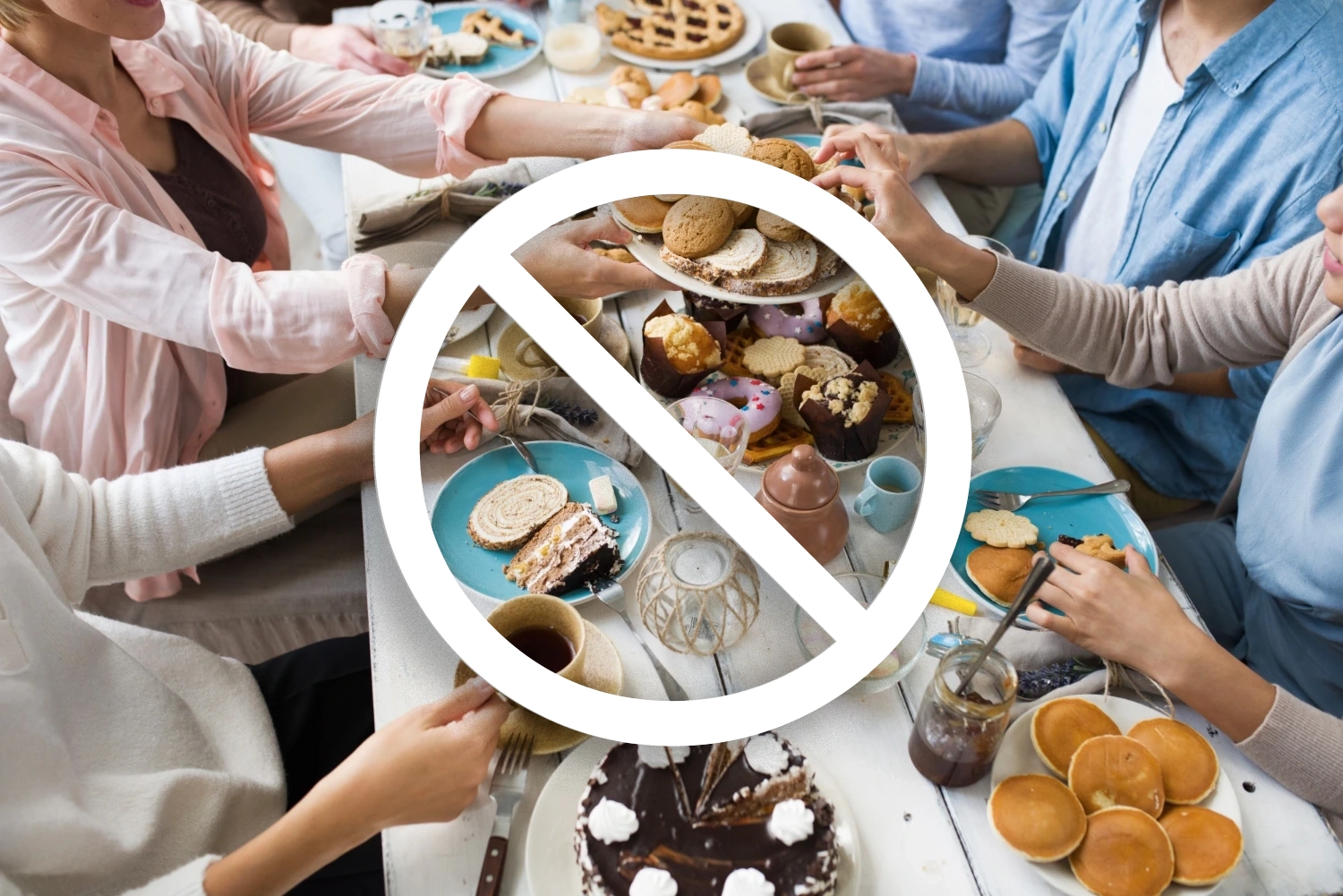 Mesa vista desde arriba llena de pasteles y postres con un símbolo de prohibición indicando evitar alimentos azucarados.