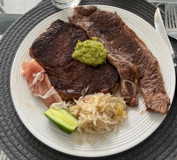 Plato con filetes de carne asada acompañados de jamón serrano, chucrut, pepino y una porción de guacamole al centro.