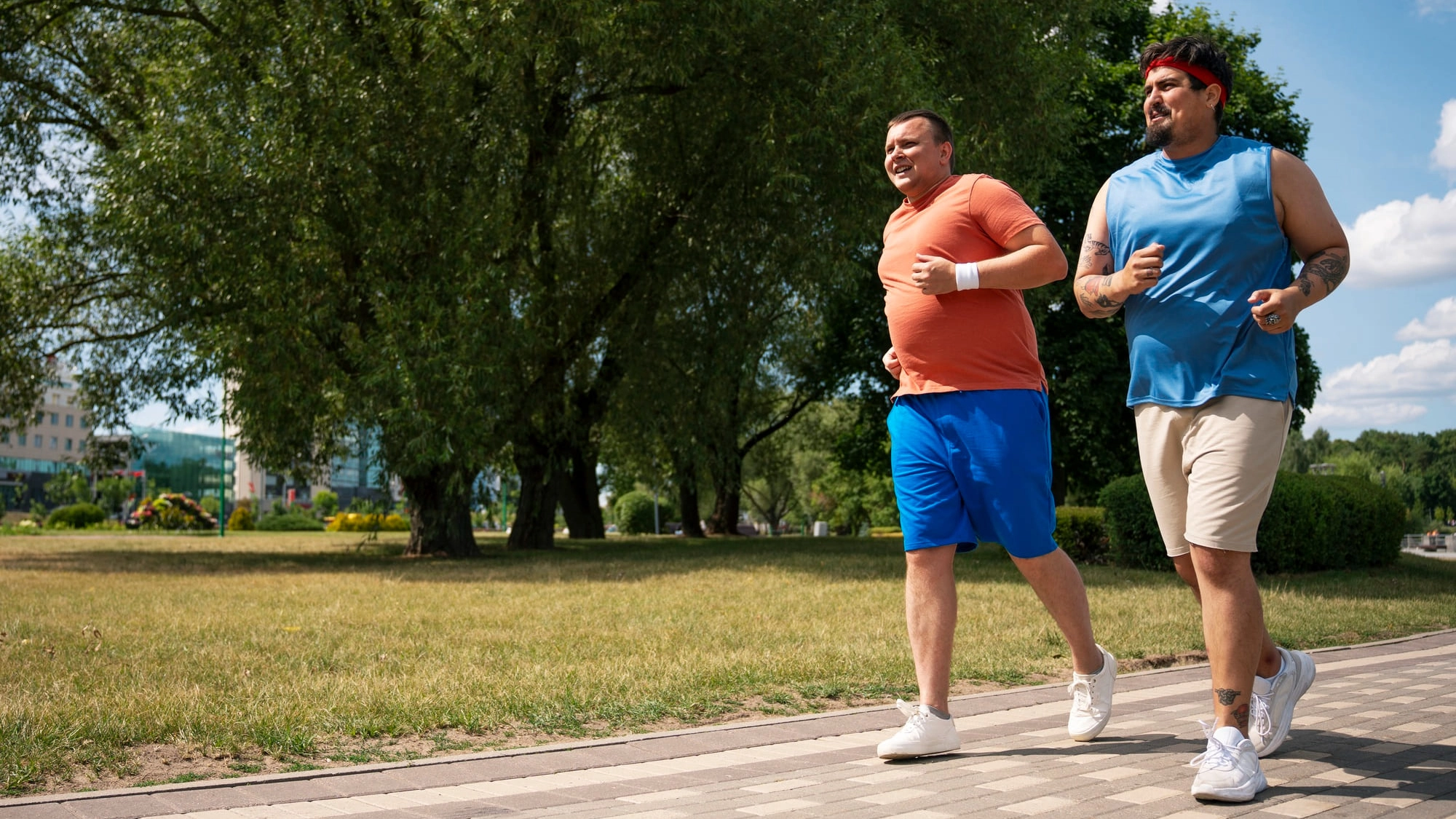 Dos hombres con sobrepeso corriendo al aire libre en un parque, iniciando una rutina de ejercicio para mejorar su salud.