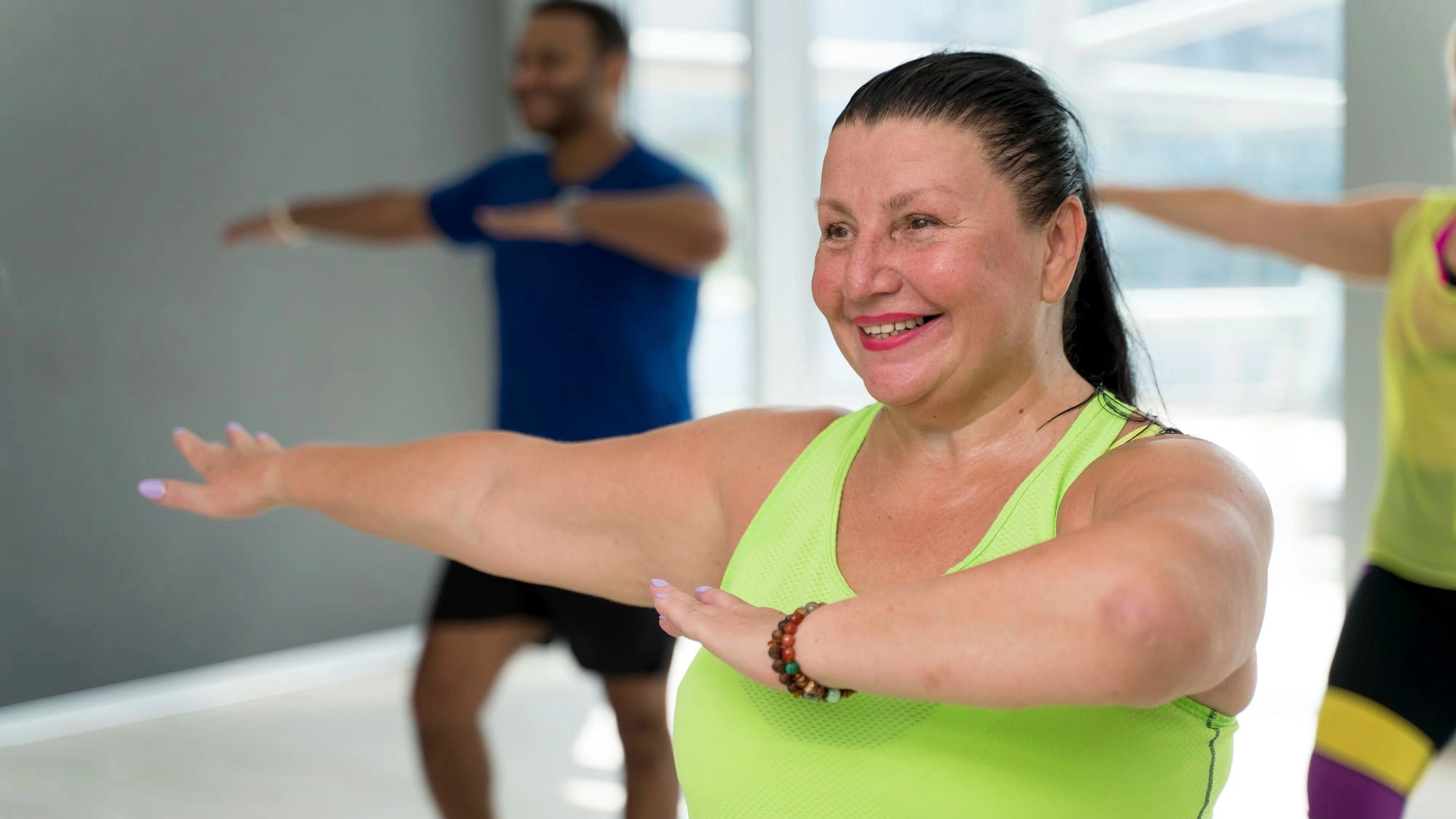Mujer sonriente realizando ejercicios de brazos en una clase grupal de actividad física en interior.