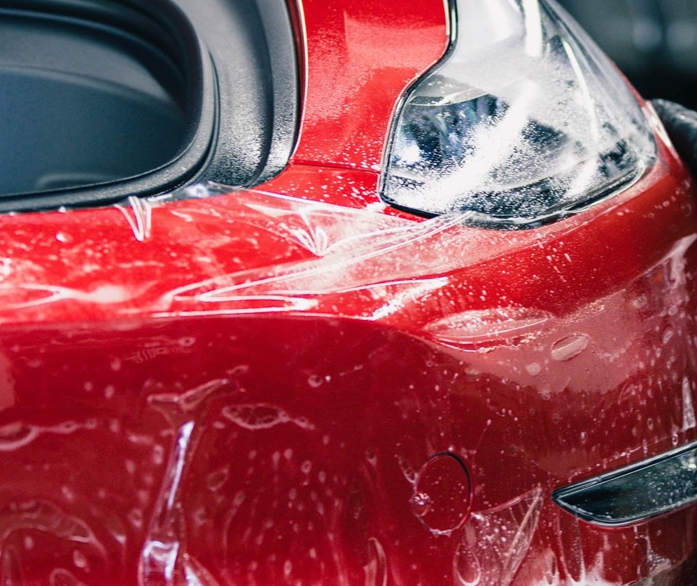 An American Auto Connection installer laying paint protection film onto a front fender