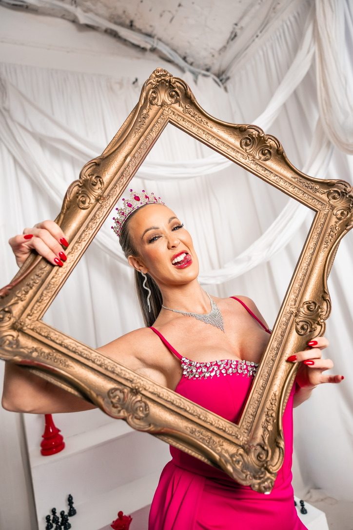 Nurse Kim in a pink dress and tiara, holding a gold picture frame