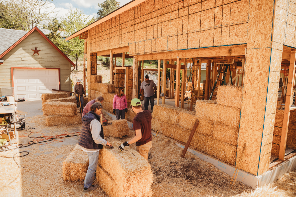 Workers stacking straw bales during construction of seismic-resistant custom home in Idaho