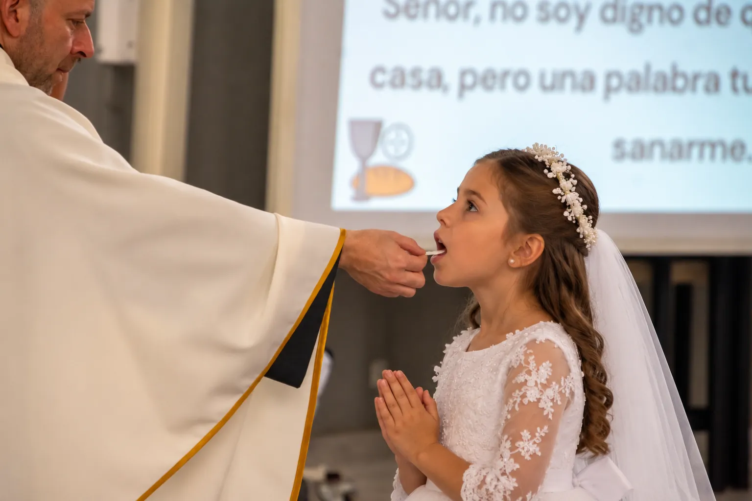 Una niña recibe la Primera Comunión de manos de un sacerdote