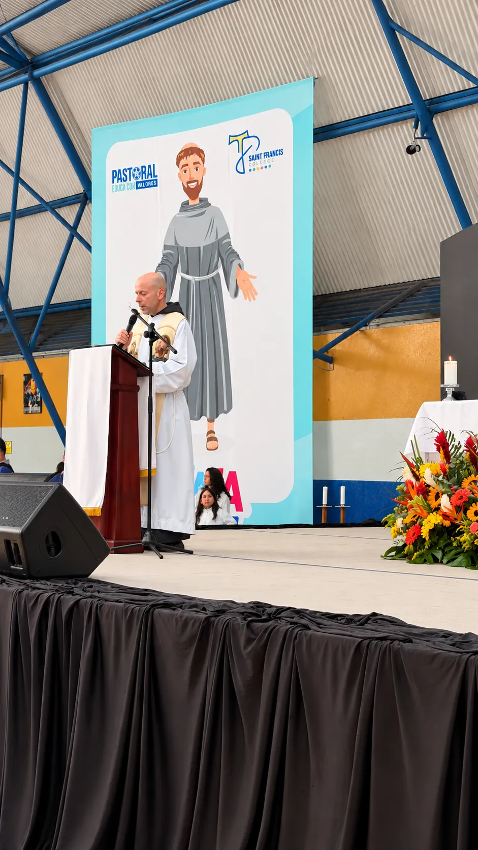 Un fraile habla desde el escenario en una ceremonia de Pastoral del colegio