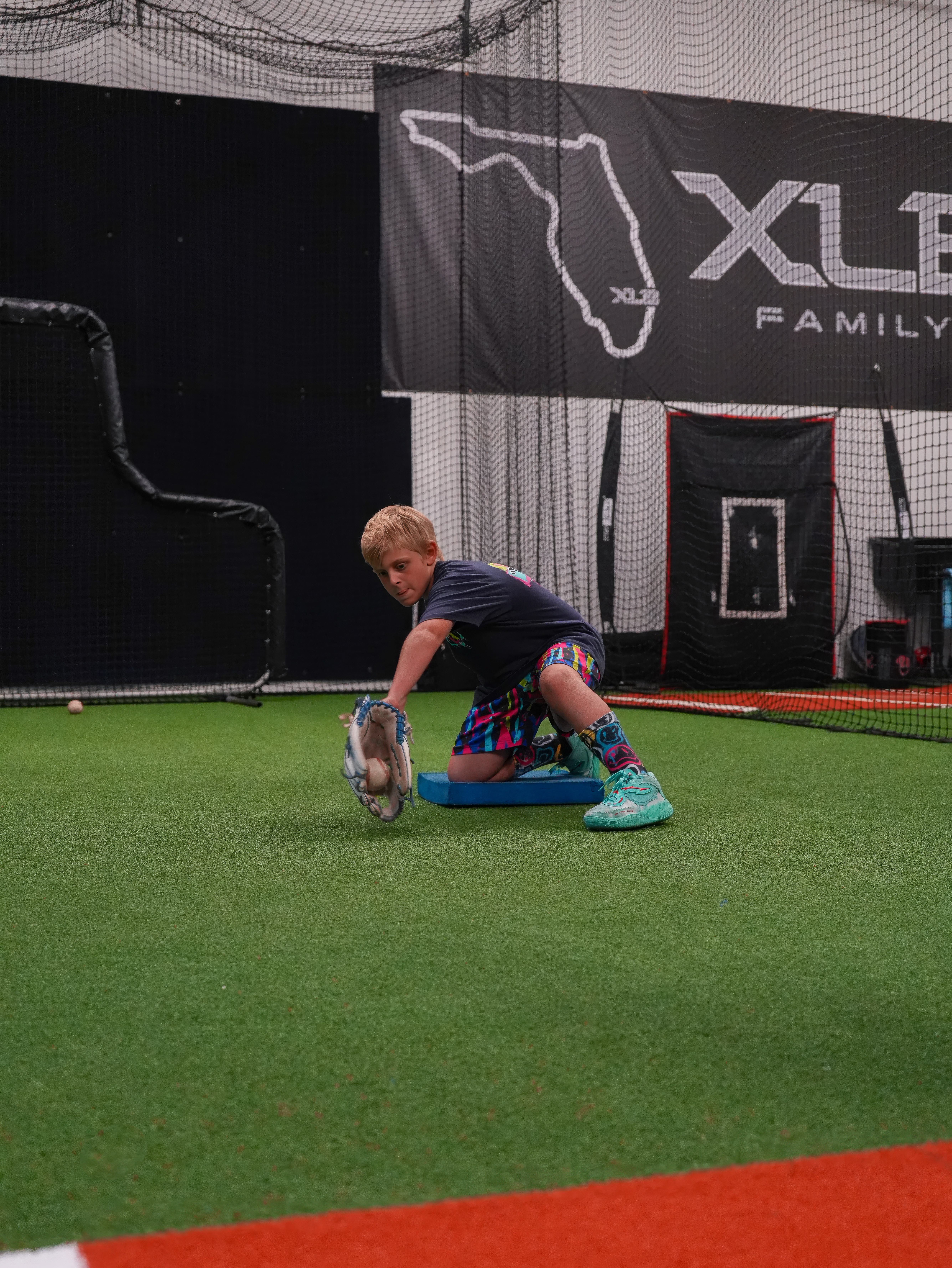 XLB Training coach running ground ball reps with a youth infielder on the indoor turf