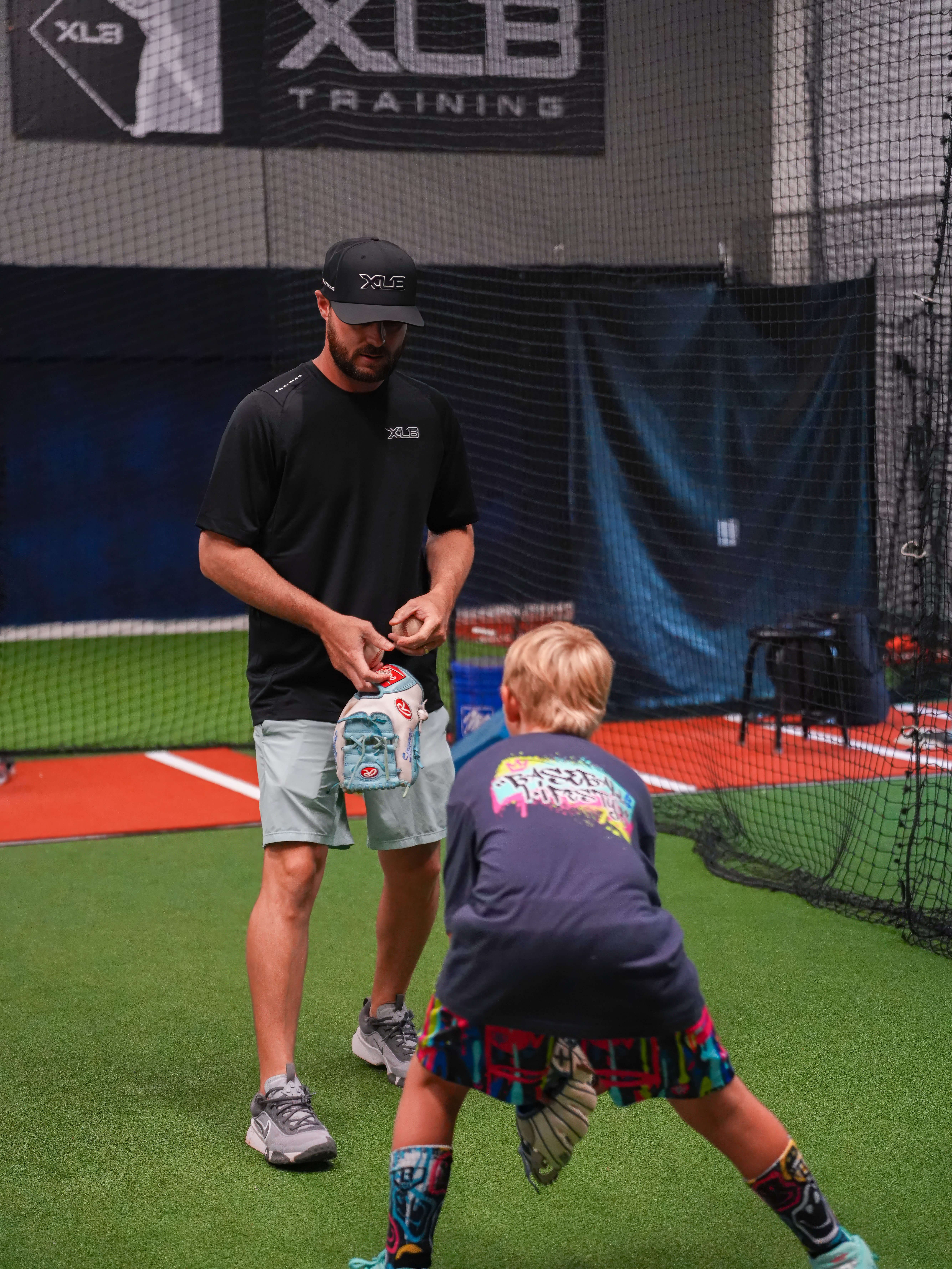 An XLB Training coach teaching a young player a baseball grip during a youth baseball camp in Boynton Beach, Florida