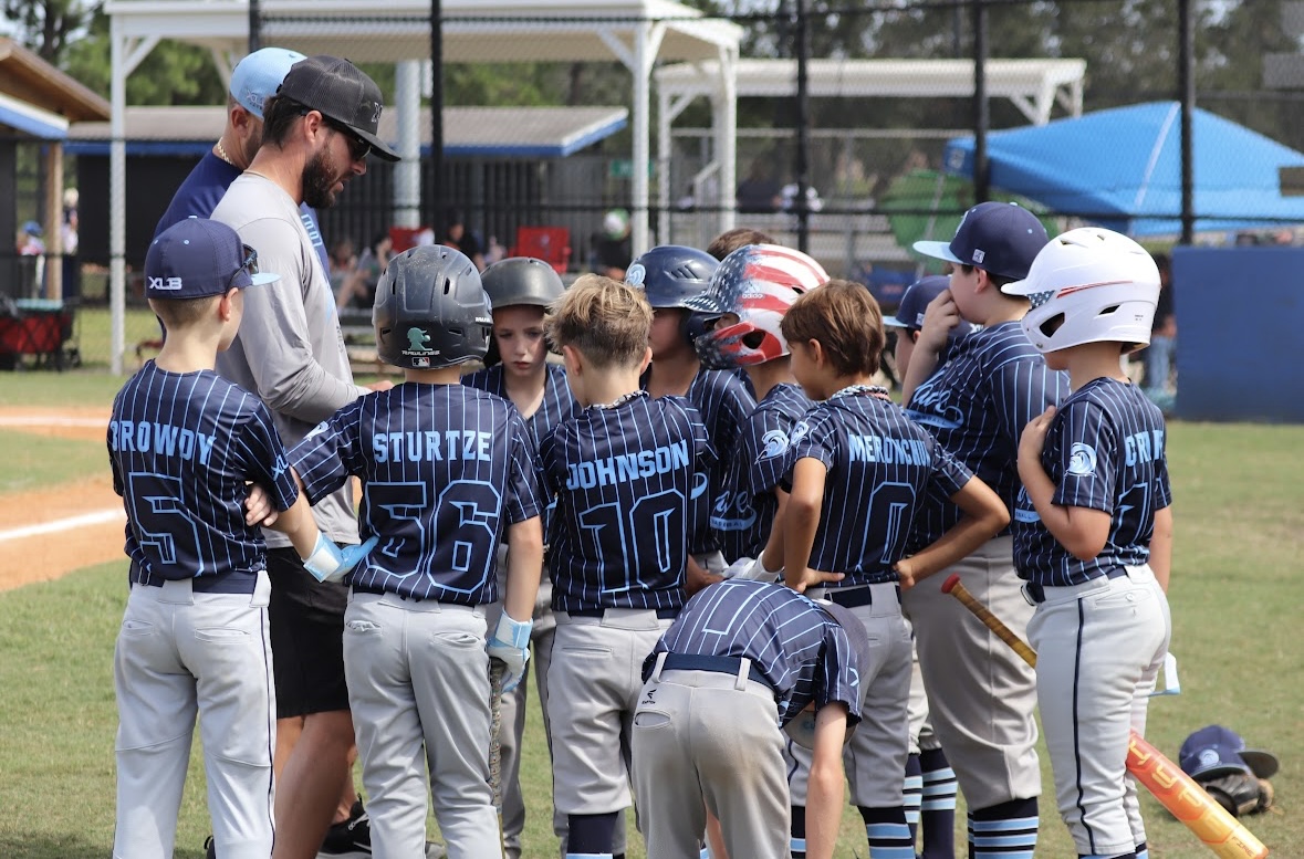 An XLB Wave coach leading a team huddle with youth travel baseball players in Boynton Beach, Florida