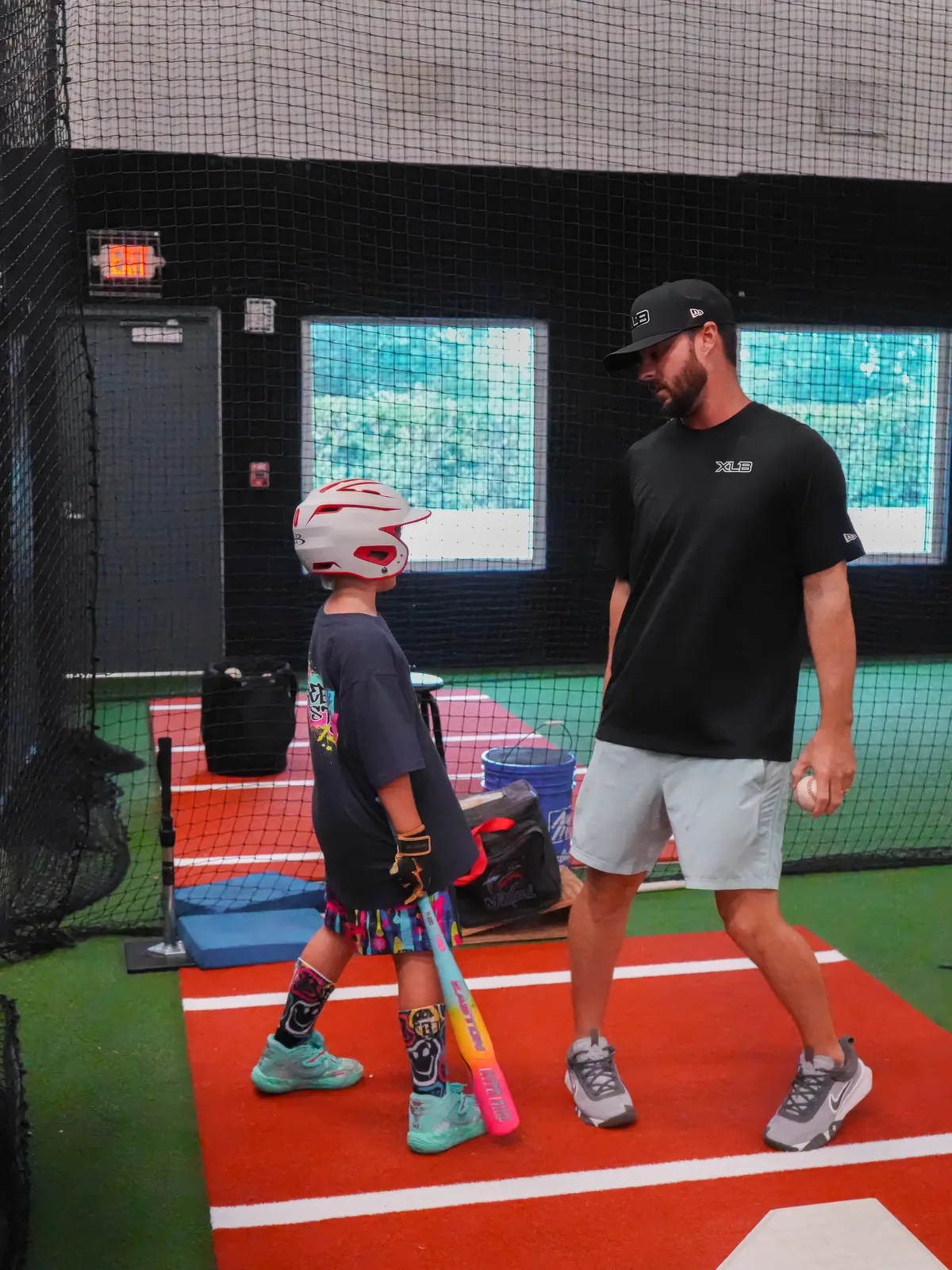 XLB Training coach giving one-on-one hitting instruction to a young player in the cage in Boynton Beach