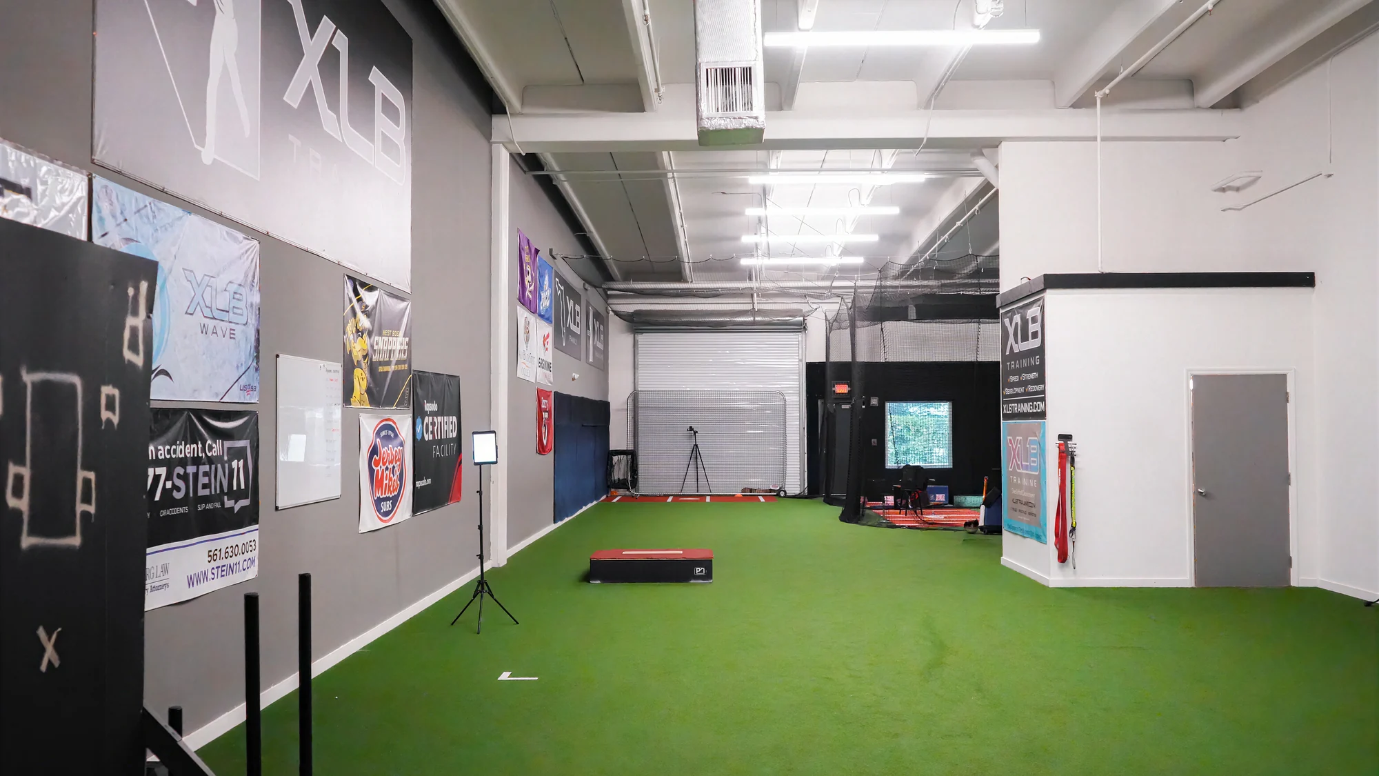 Interior of the XLB Training baseball facility in Boynton Beach, Florida, with indoor turf, batting cages, and a pitching lane